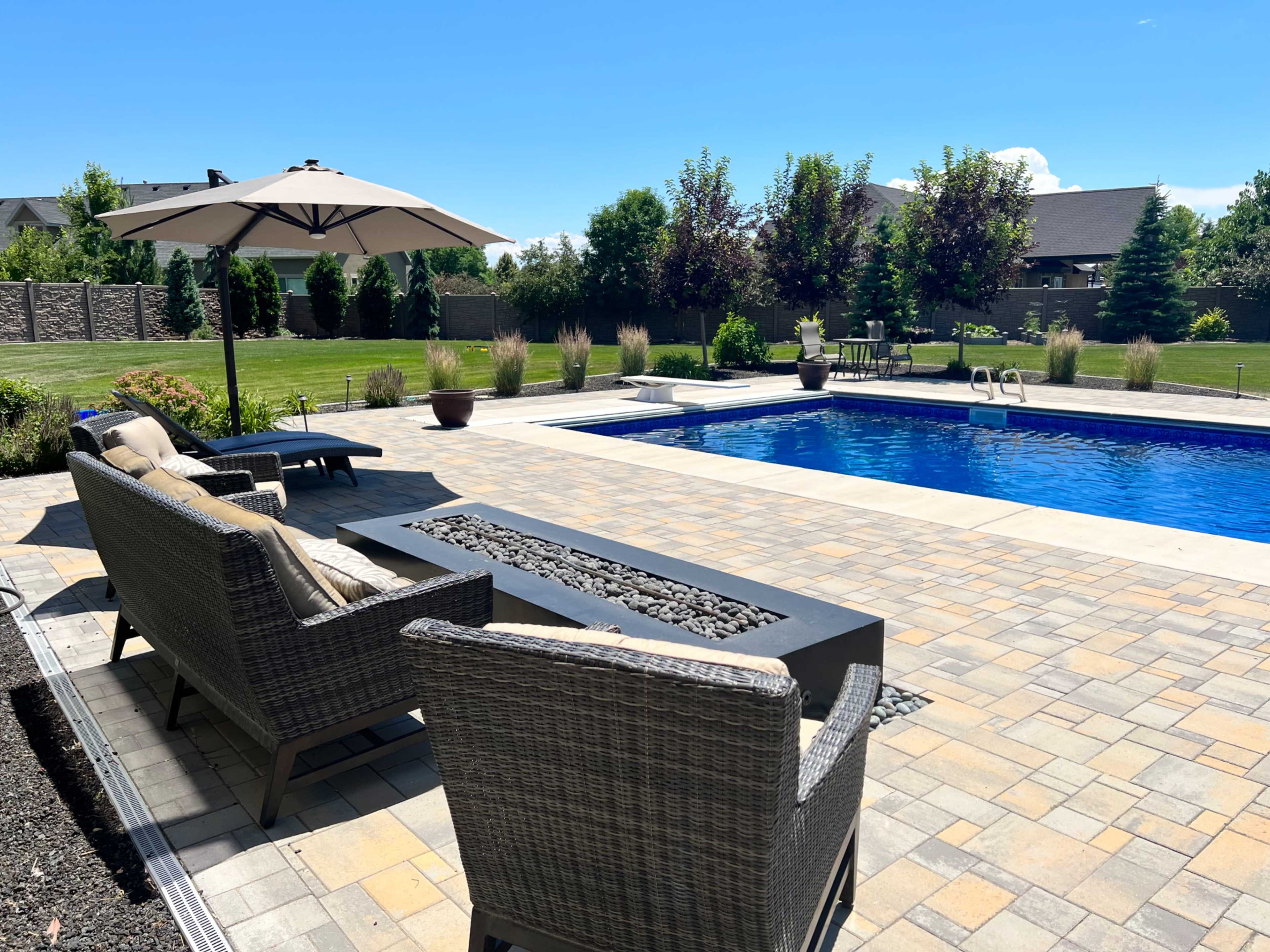 A patio area with two chairs and a table overlooks a blue swimming pool surrounded by greenery and landscaping.