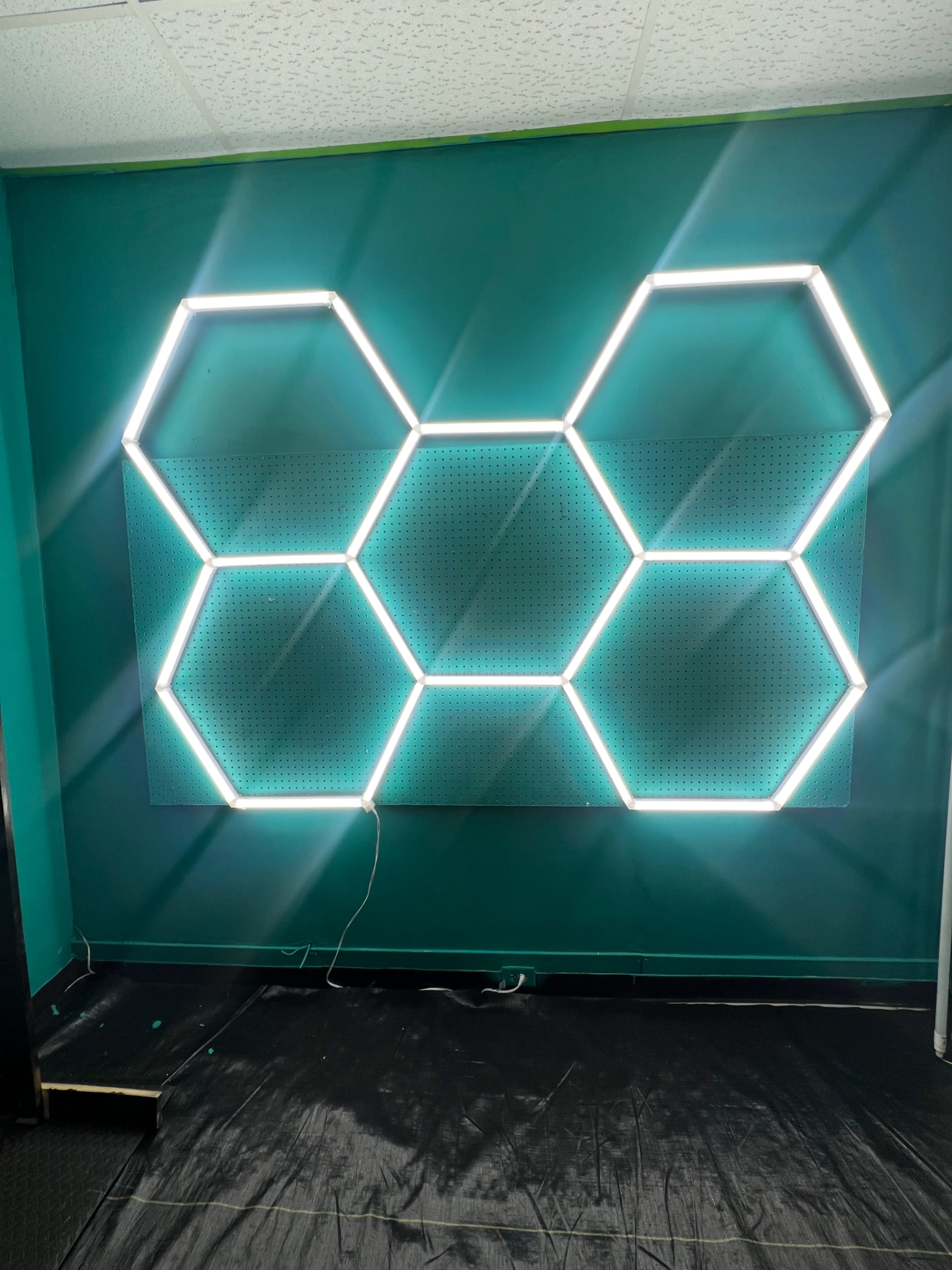The image shows a teal wall with a large hexagonal light display made up of several illuminated panels.