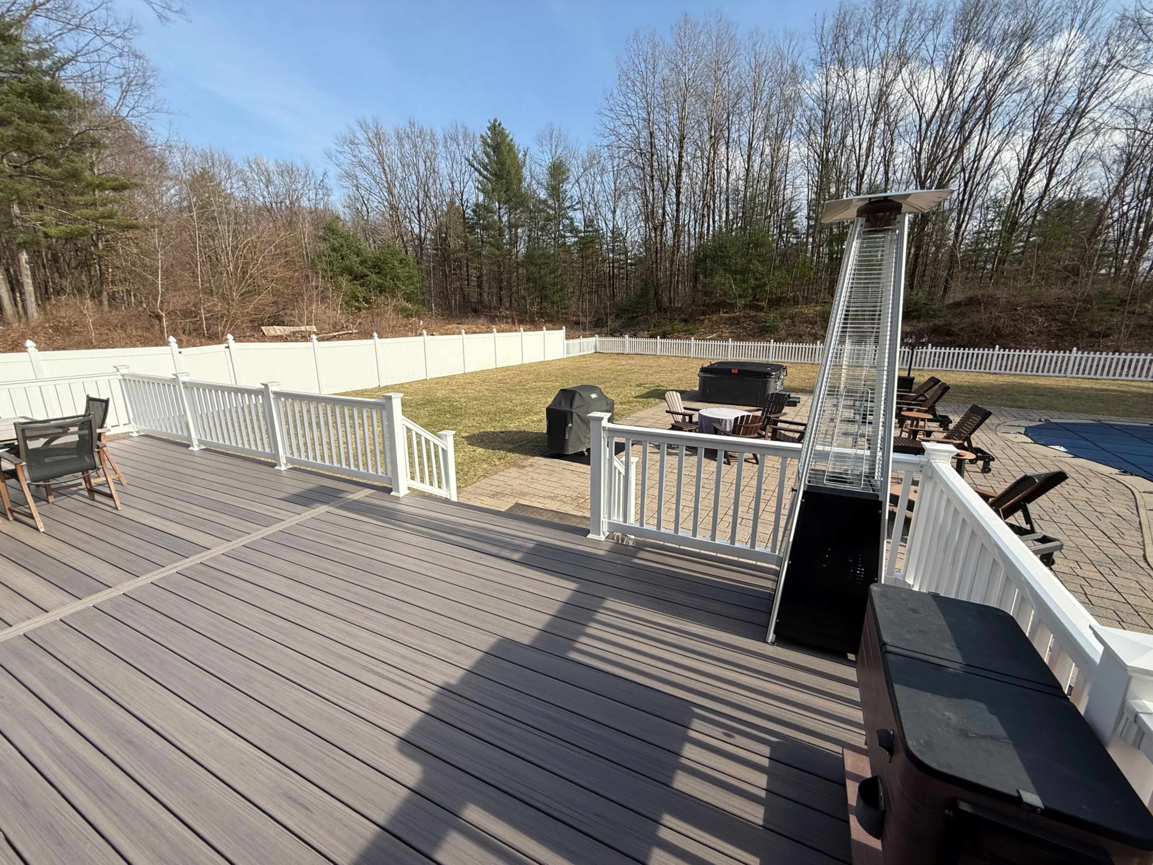 A spacious deck overlooks a grassy area and a pool, with a patio heater and various outdoor furniture arranged nearby.