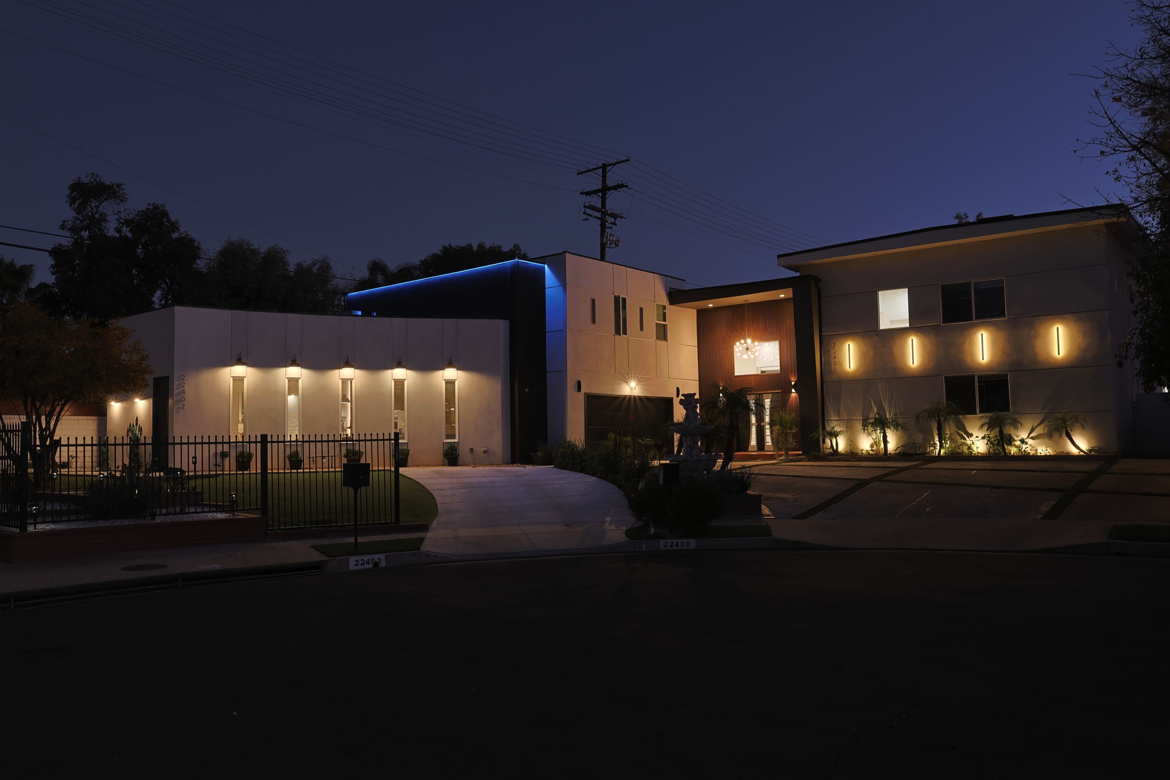 A modern building at night features illuminated facades and a landscaped entrance.
