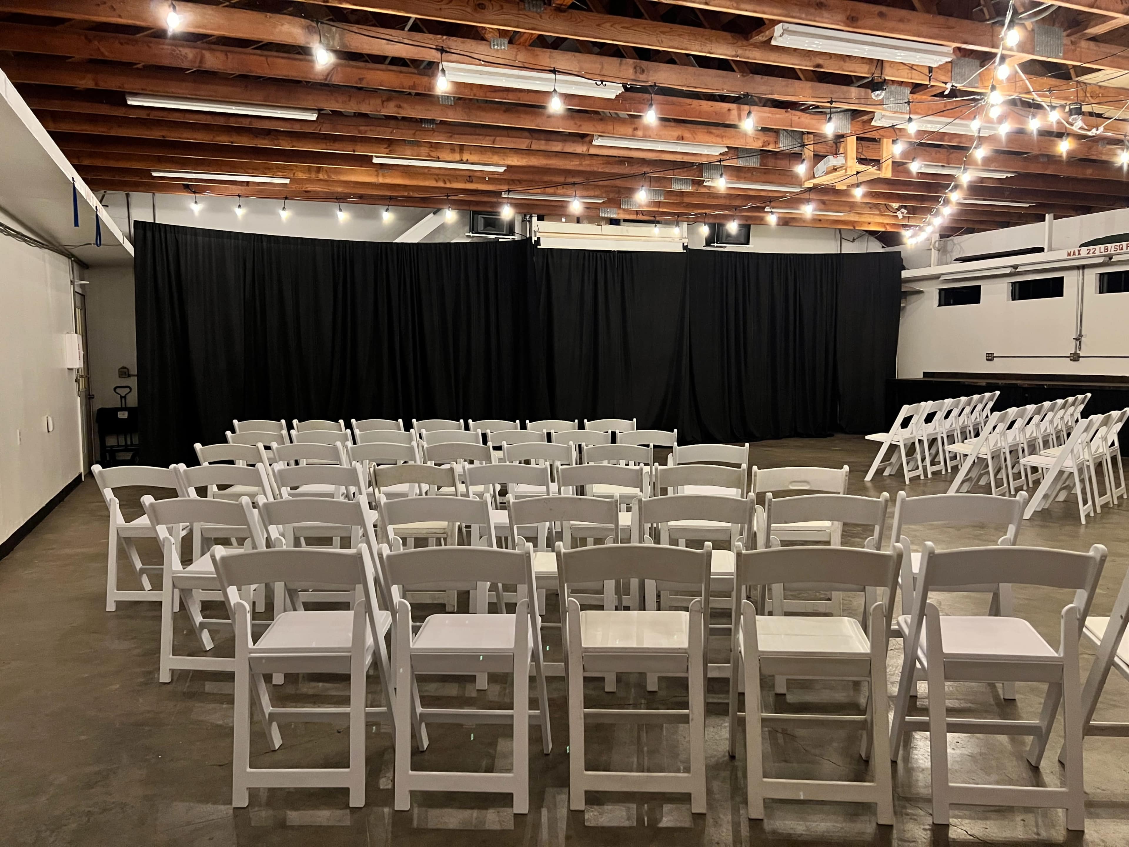 A room with a stage separated by black curtains and rows of white chairs arranged for an event.