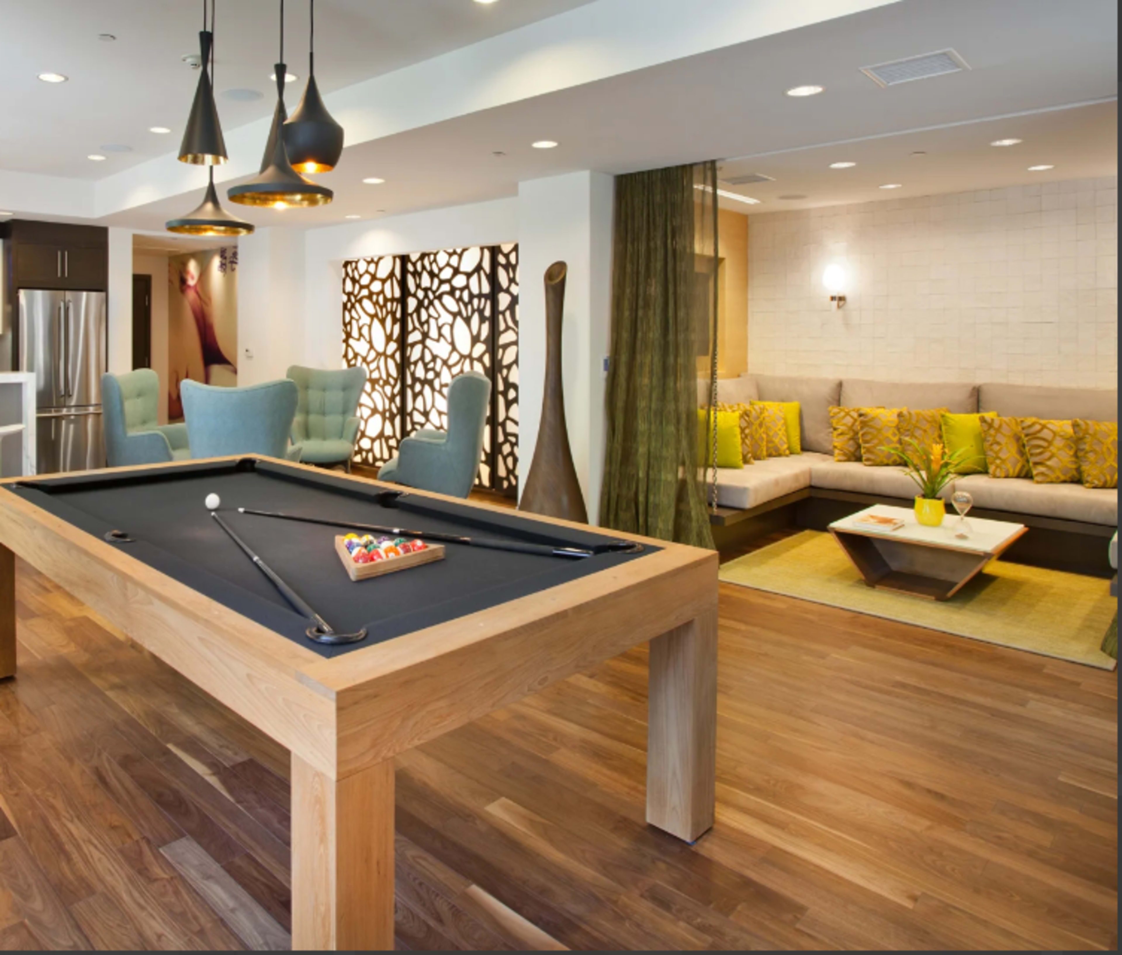 A modern lounge area featuring a wood pool table, comfortable seating, and decorative wall panels.