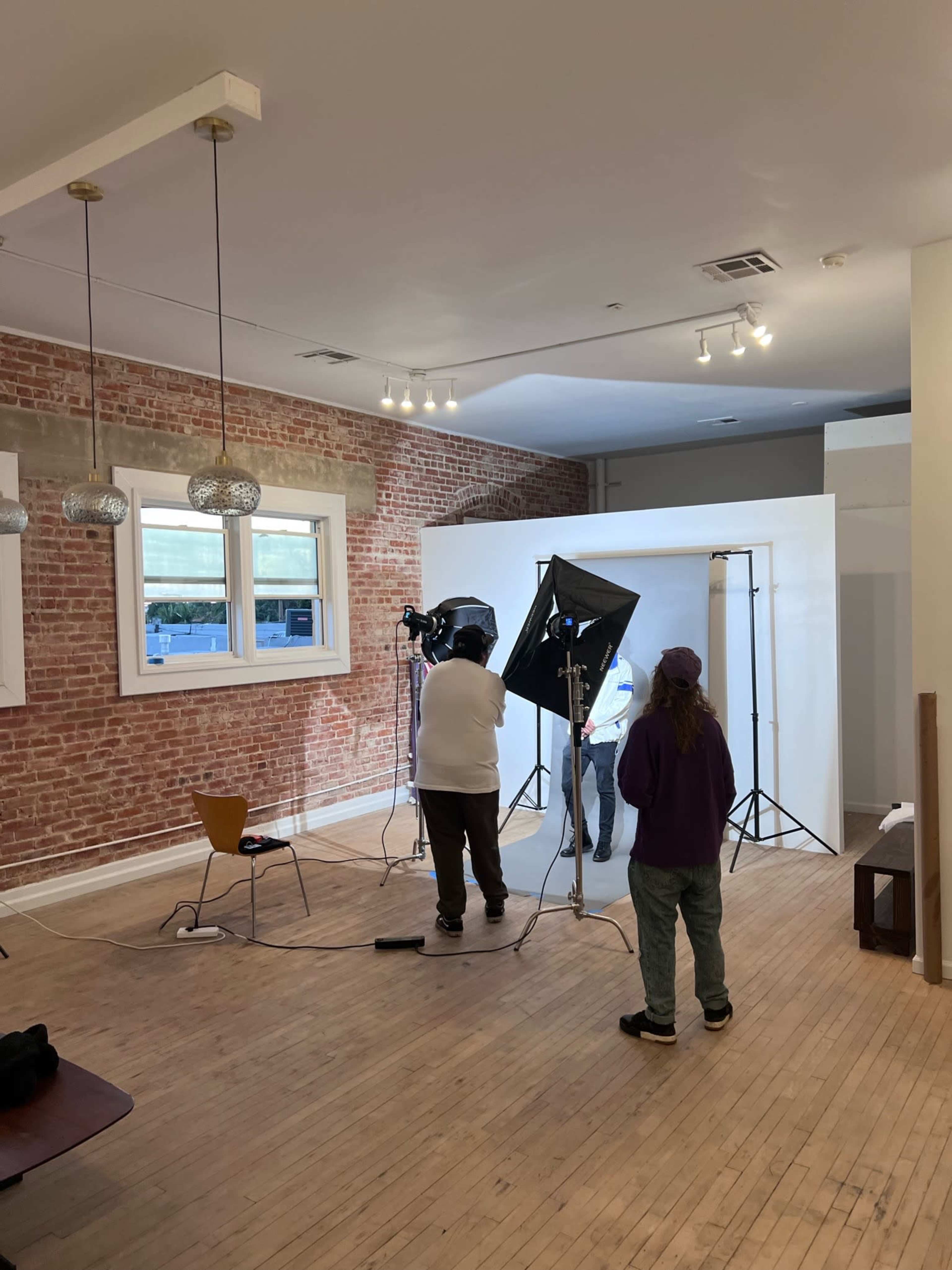 A photography studio is set up with a backdrop, lighting equipment, and two individuals preparing for a shoot.