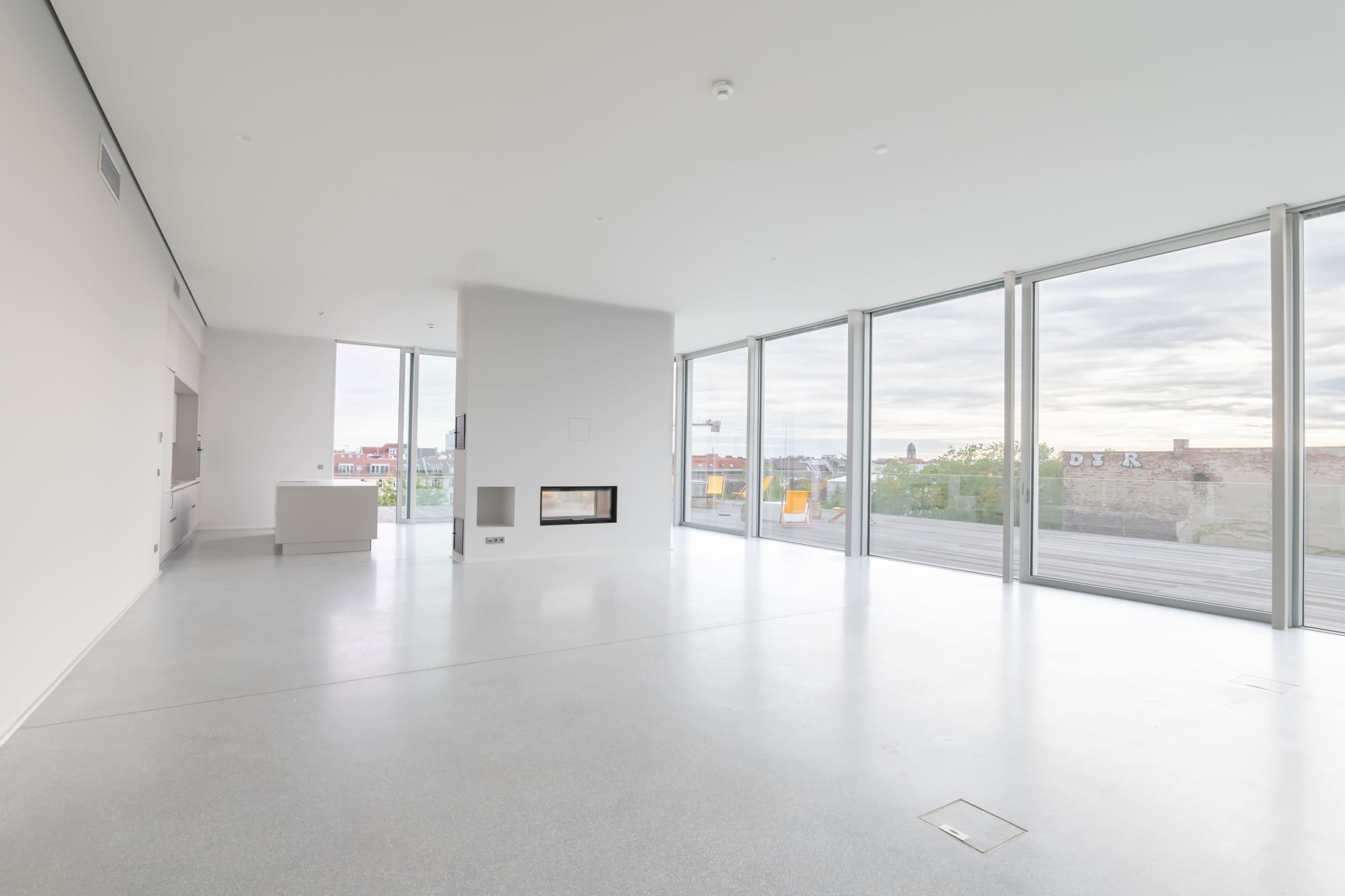 The image shows a minimalist interior of a modern room with large glass windows and a white wall-mounted fireplace.