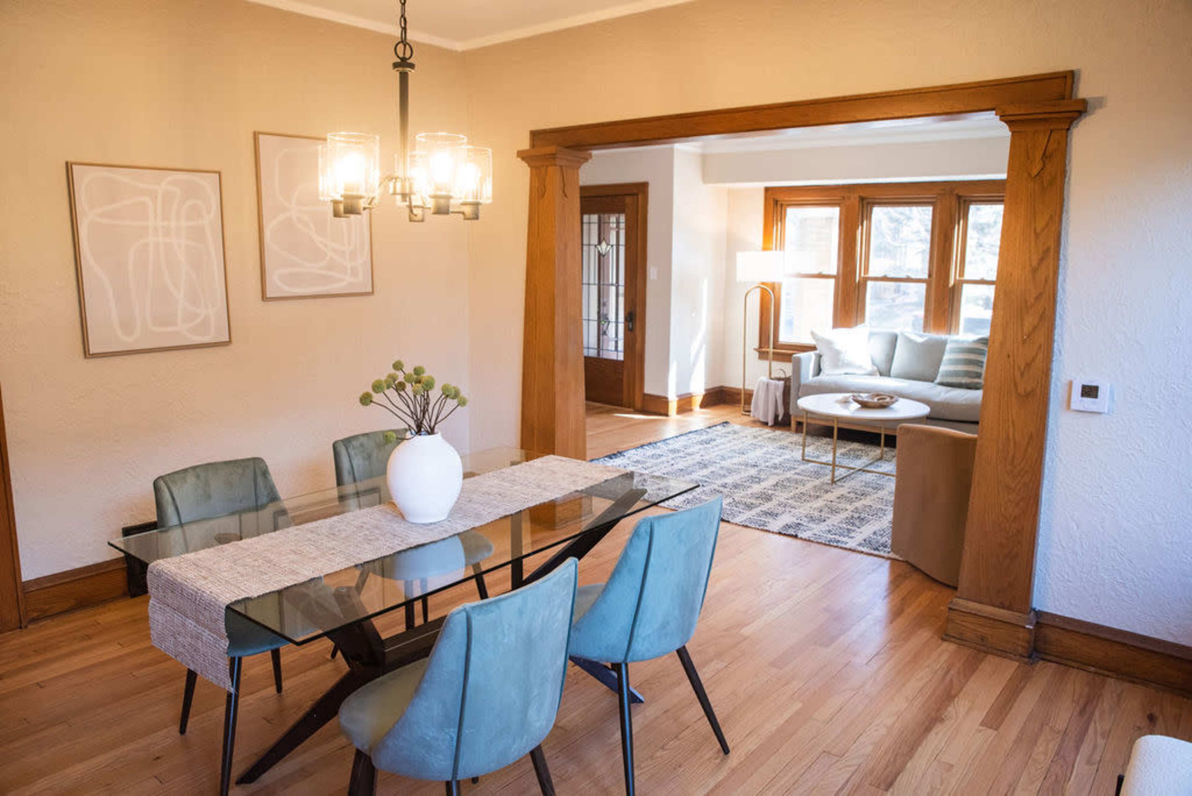 A dining area with a glass table and teal chairs is adjacent to a living room featuring a sofa and a coffee table.