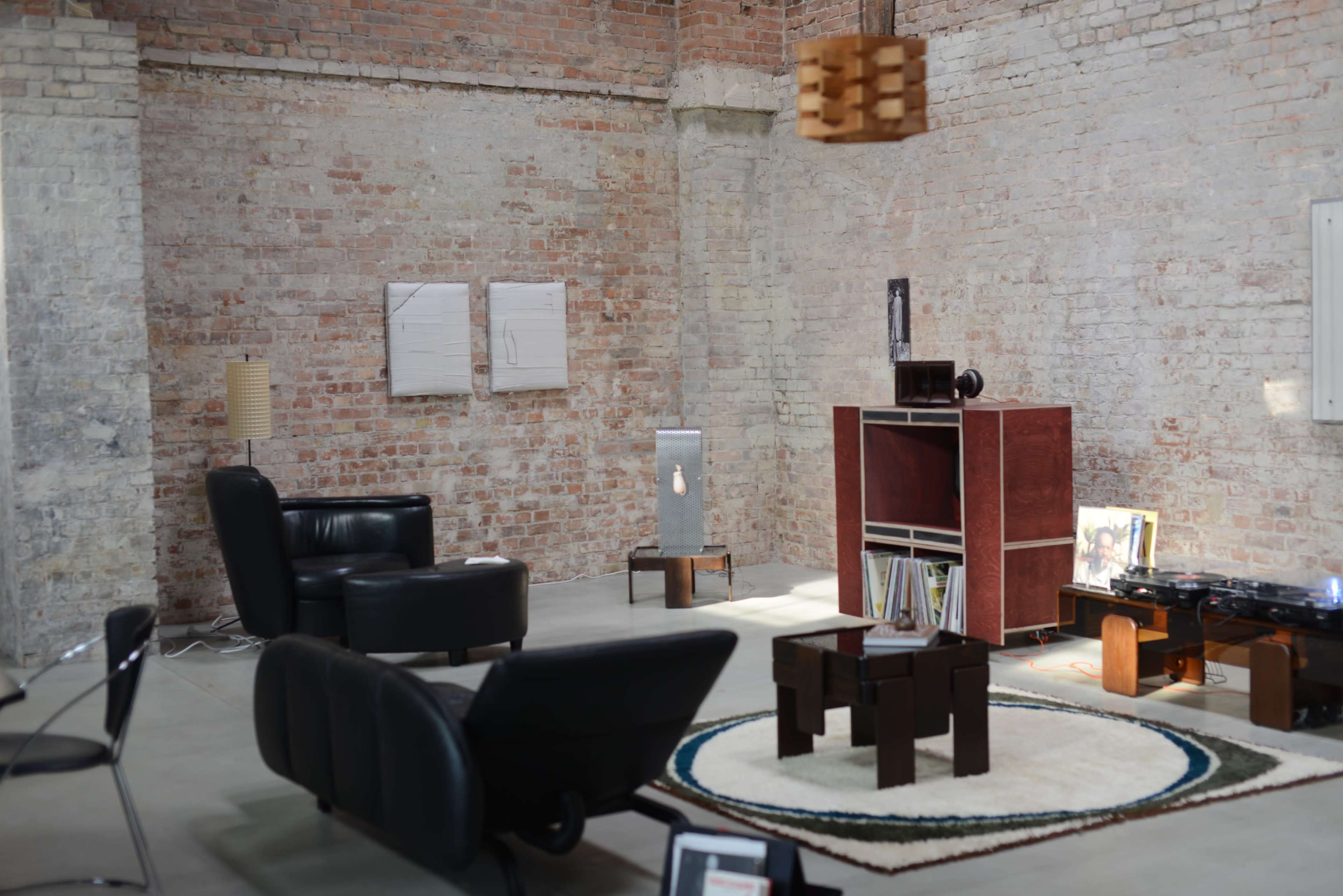 A modern living space features brick walls, minimalist furniture, and a circular rug, with artwork displayed on the walls.