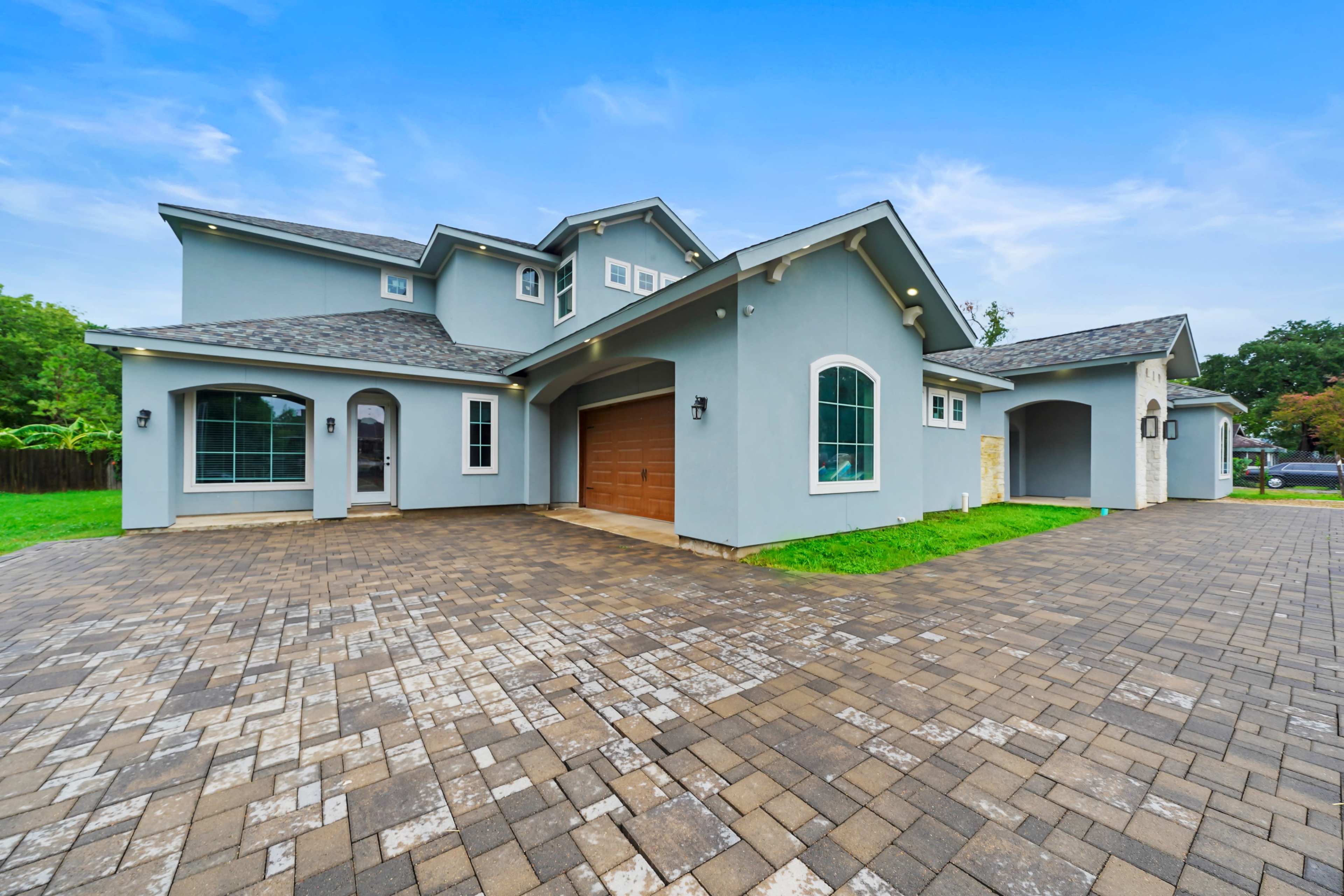 The image shows a modern two-story house with a gray exterior, a brick-paved driveway, and well-maintained landscaping.