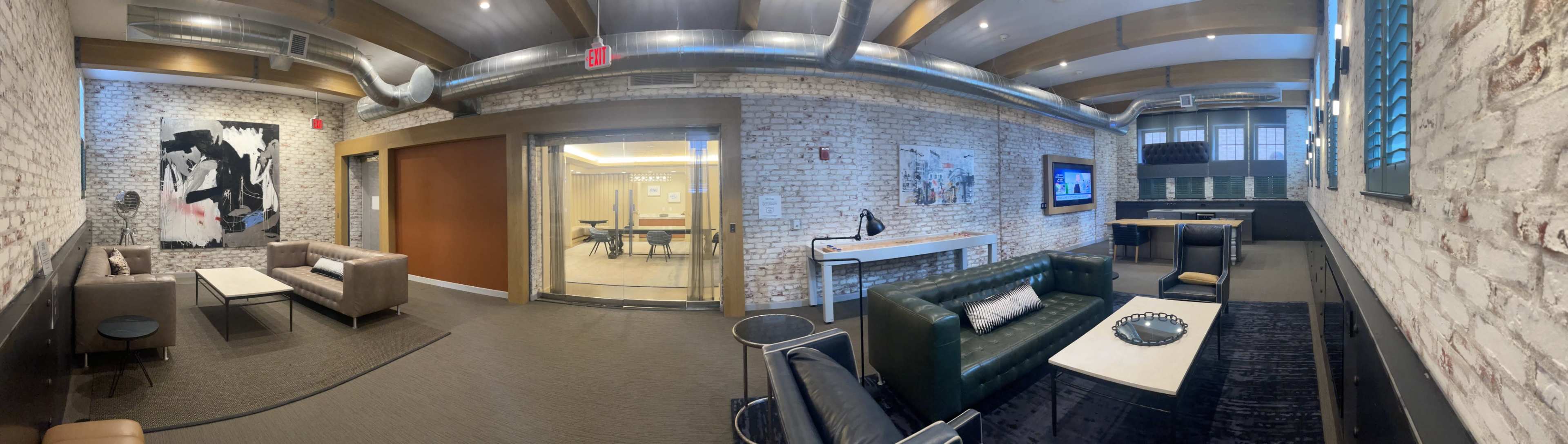 A modern office space featuring exposed brick walls, comfortable seating areas, and a conference room visible through glass doors.