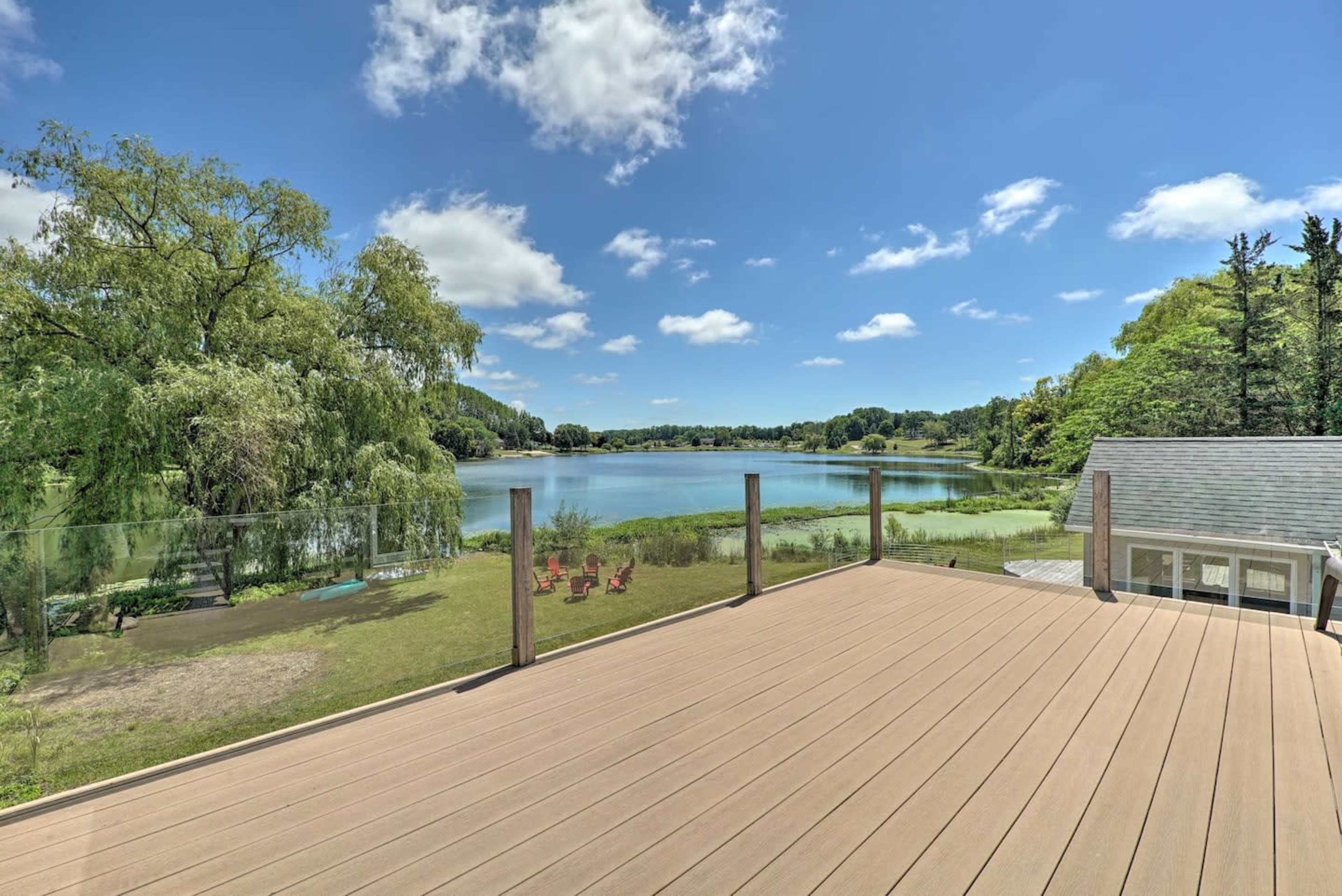 A spacious deck overlooking a calm lake surrounded by lush greenery and blue skies.