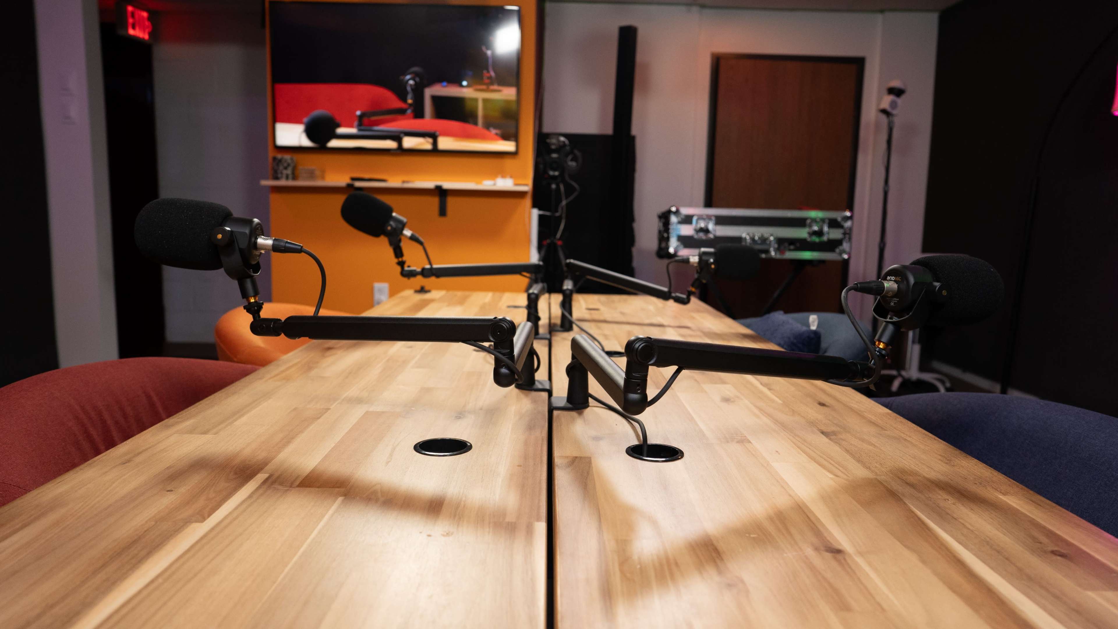 A wooden conference table with two microphones positioned at either end is set up in a recording studio space.
