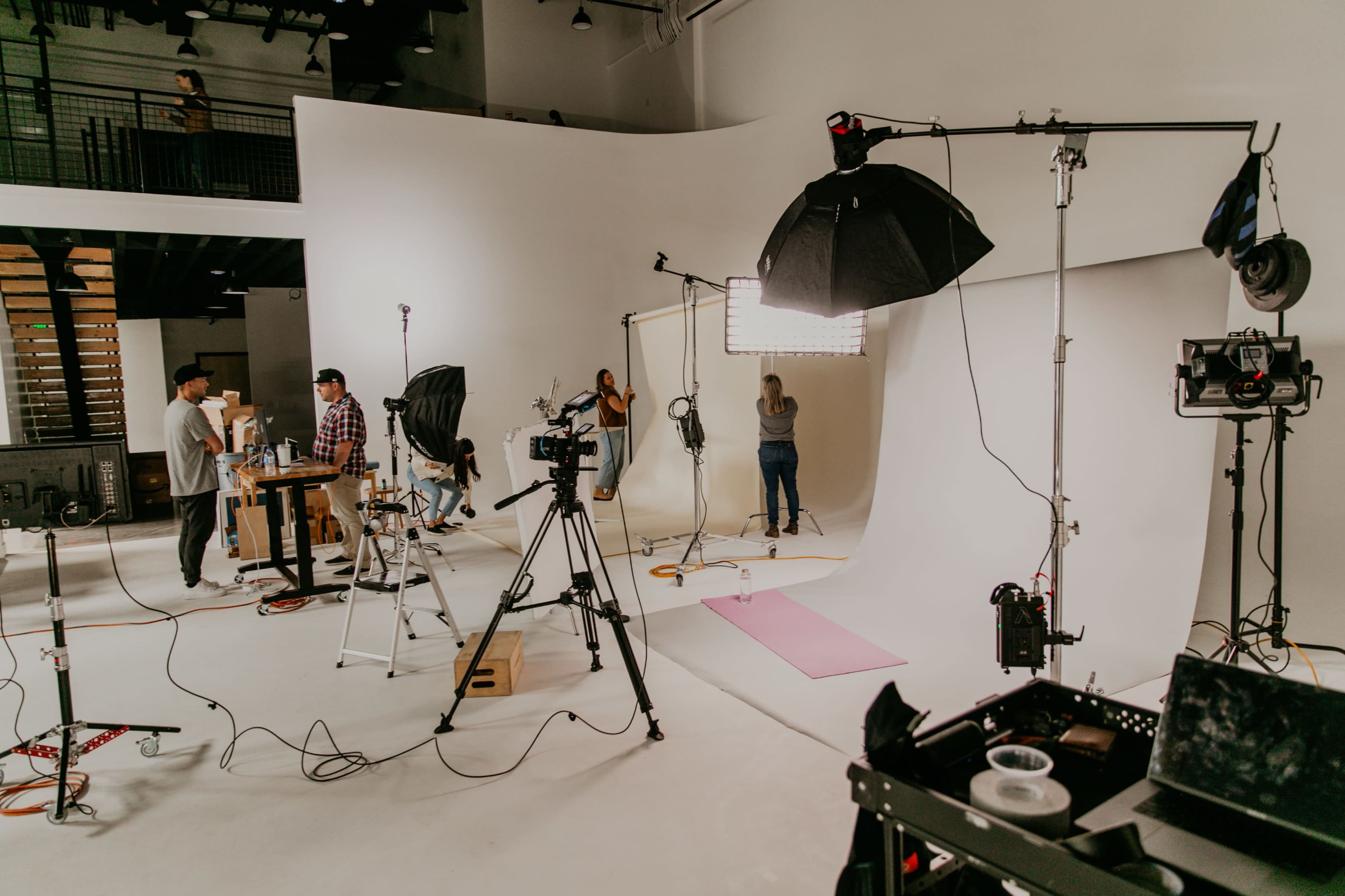 A photography studio is set up with multiple cameras, lights, and backdrops, while crew members prepare for a photoshoot.