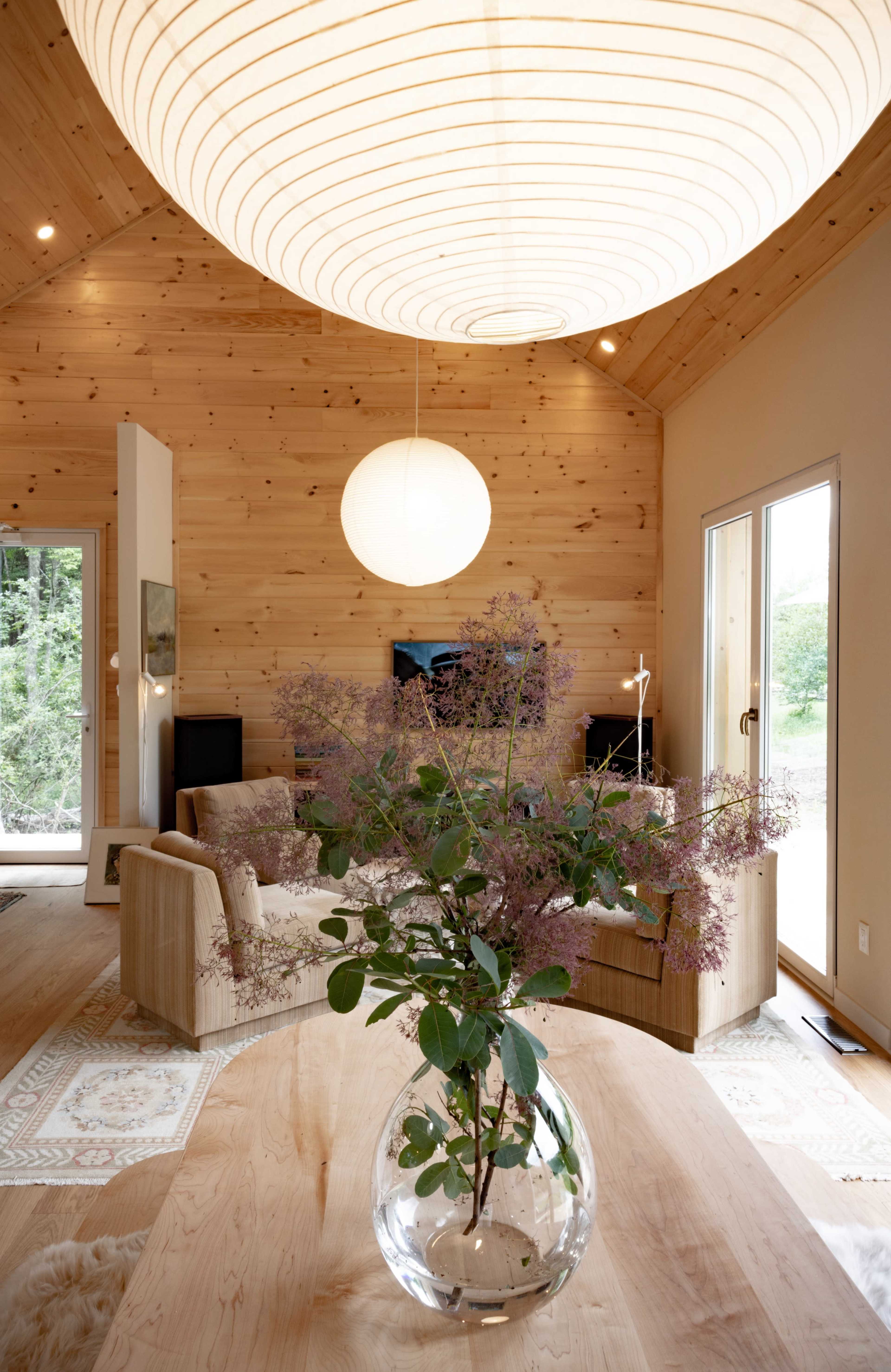 A cozy living room with wooden walls and a large round light fixture hanging from the ceiling, accompanied by a table featuring a vase of flowers.