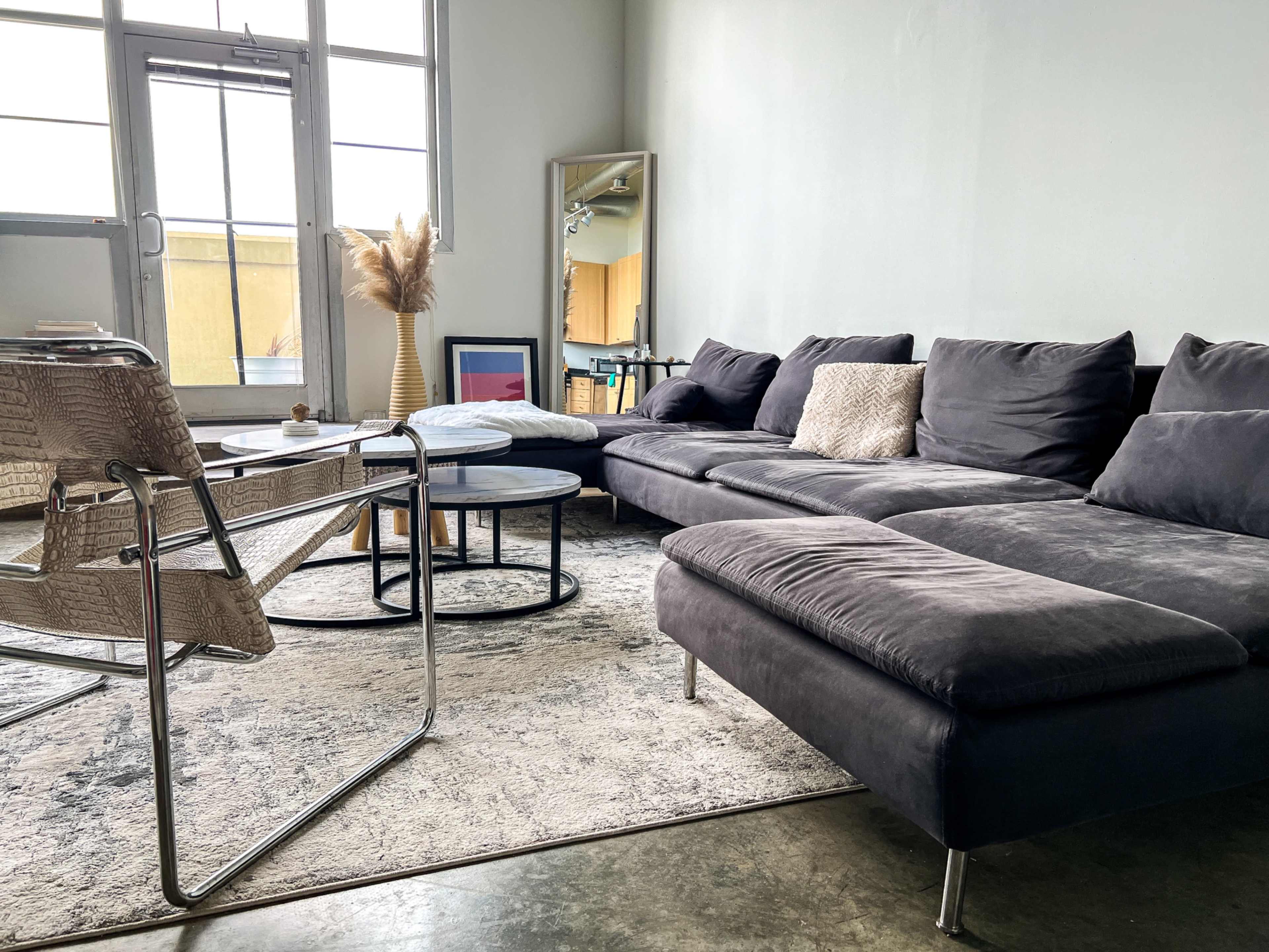 A modern living room features a gray sectional sofa, a round coffee table, a chair, and a large mirror against a light green wall.
