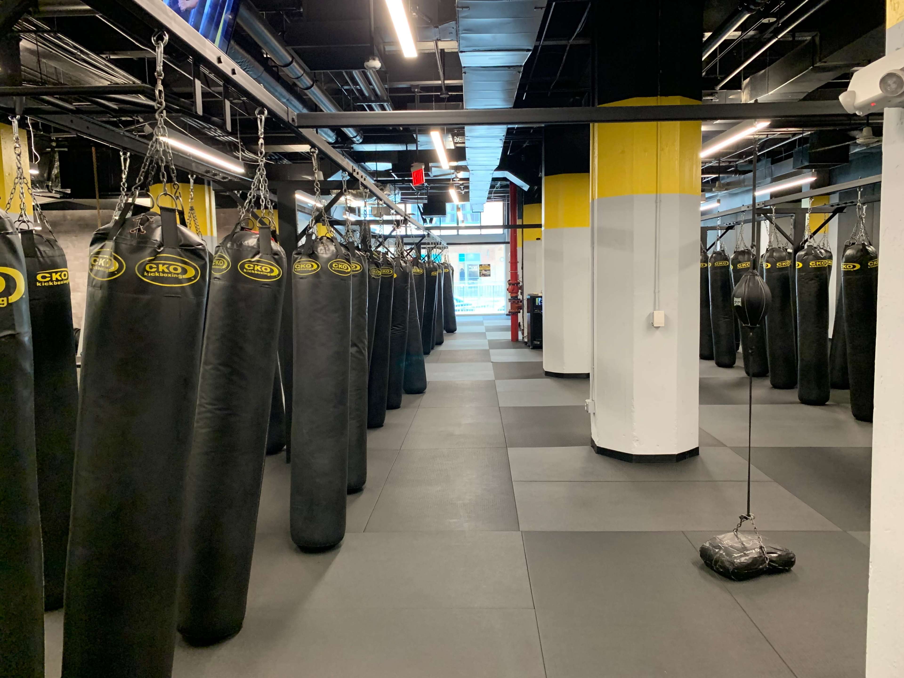 An interior gym space lined with hanging punching bags and equipped with black rubber flooring.