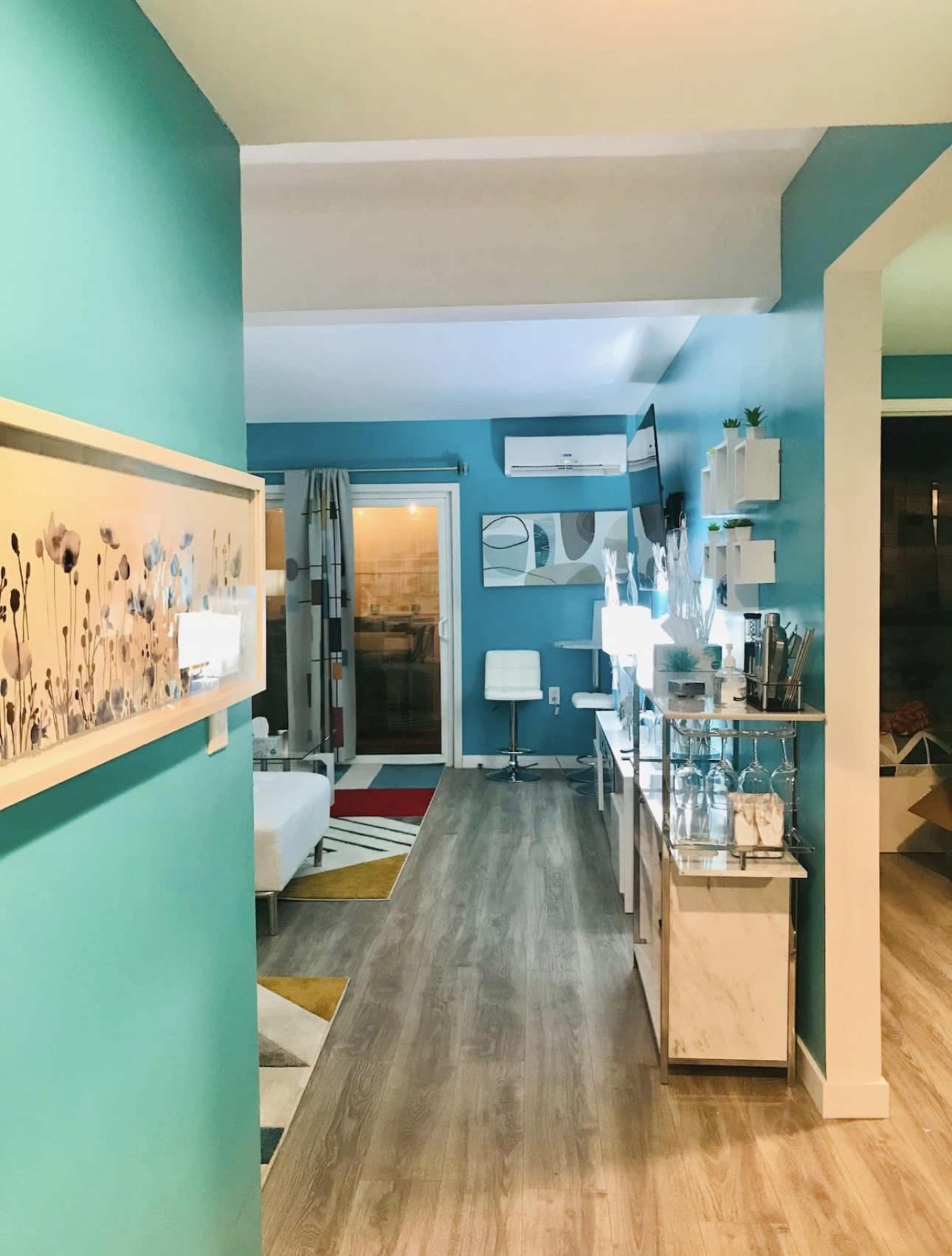 The image shows a well-lit interior hallway leading to a living area with modern decor and colorful wall art.