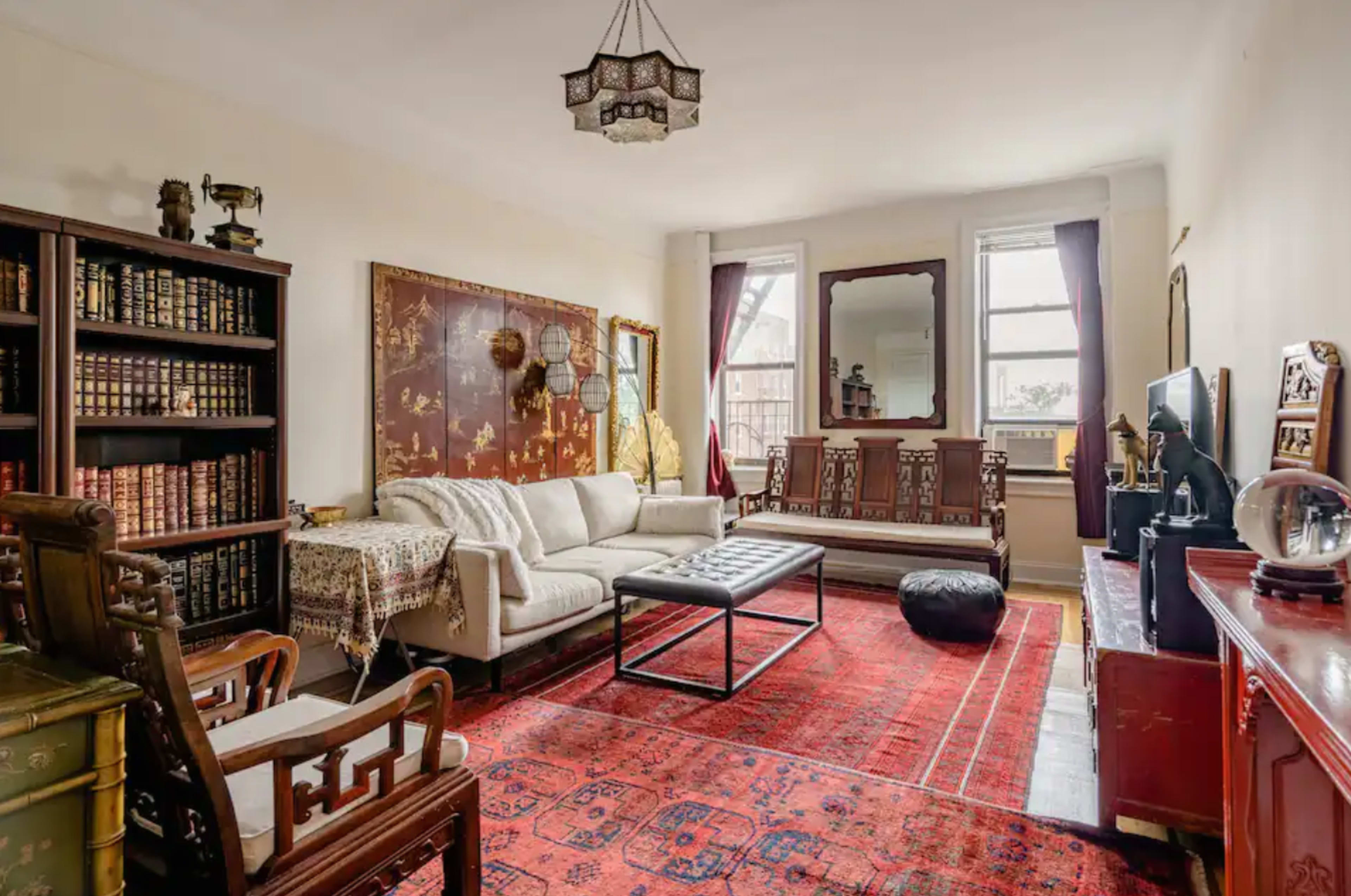 The living room features a white sofa, a coffee table, and a large red area rug, with bookshelves and decorative art on the walls.