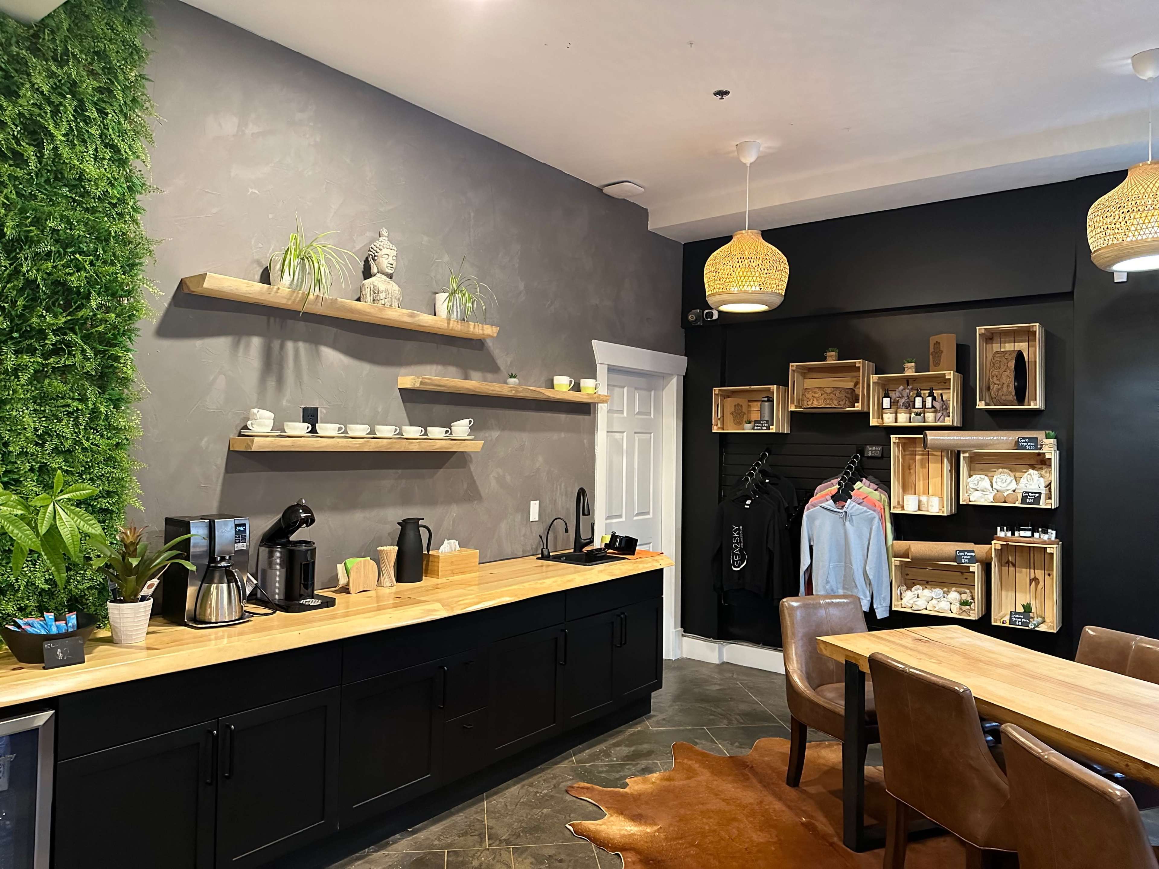 A cozy café interior with wooden shelves displaying cups and decorative items, a marble countertop with coffee equipment, and a green wall featuring plants.