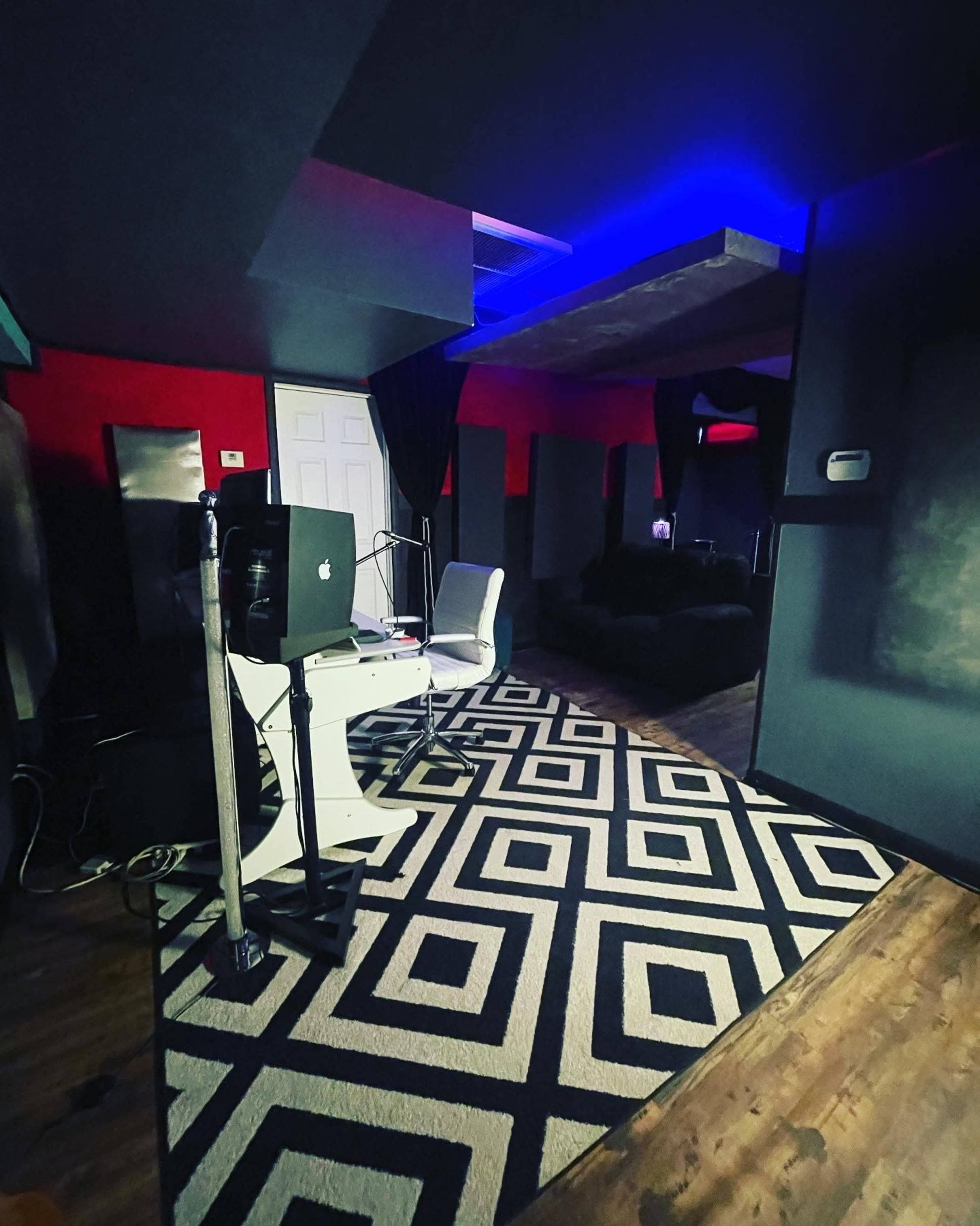 A music studio is shown with a patterned rug, black walls, and a desk featuring a computer and chair.