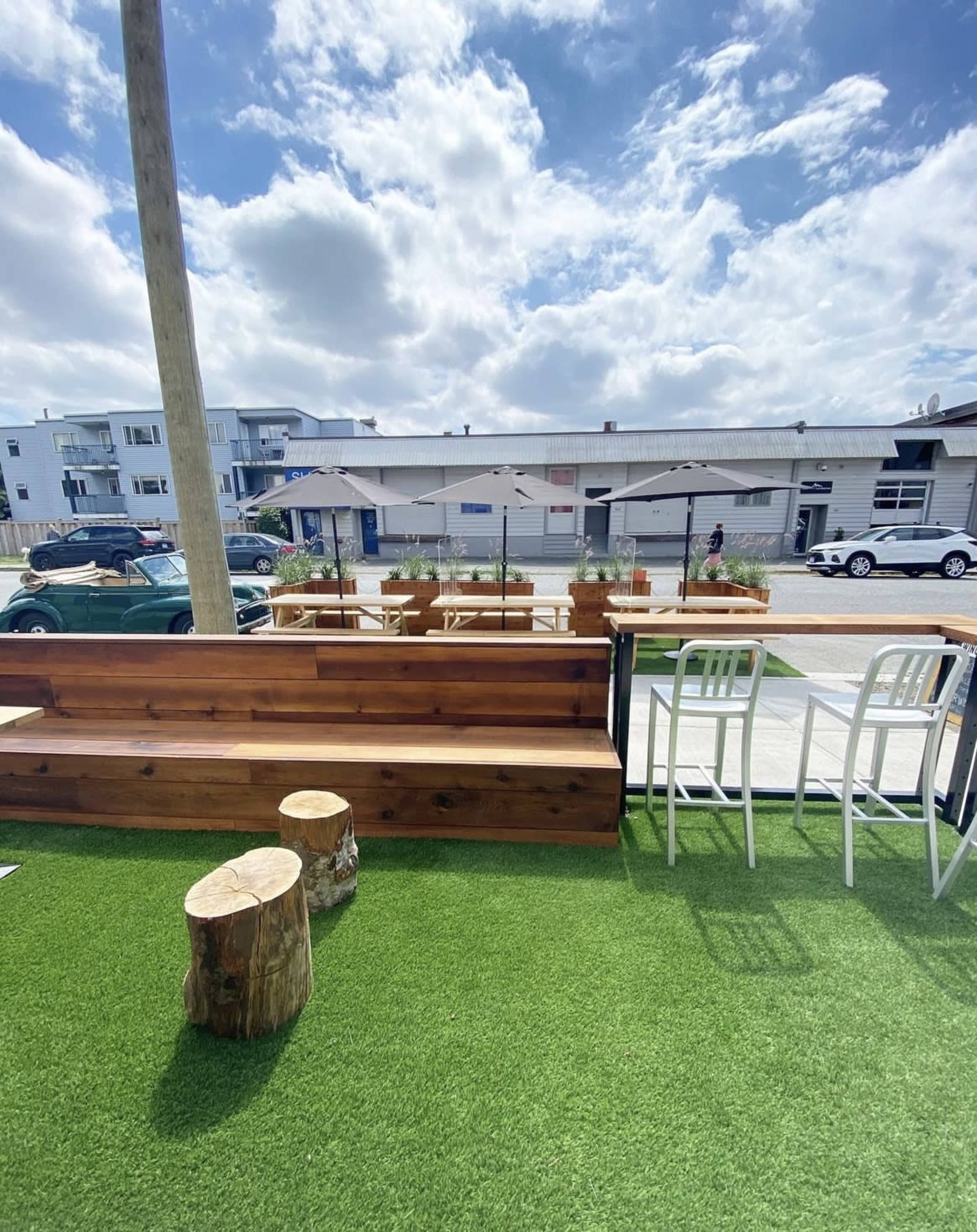 A wooden seating area on a grassy surface, with a view of a street lined with tables and umbrella shades.