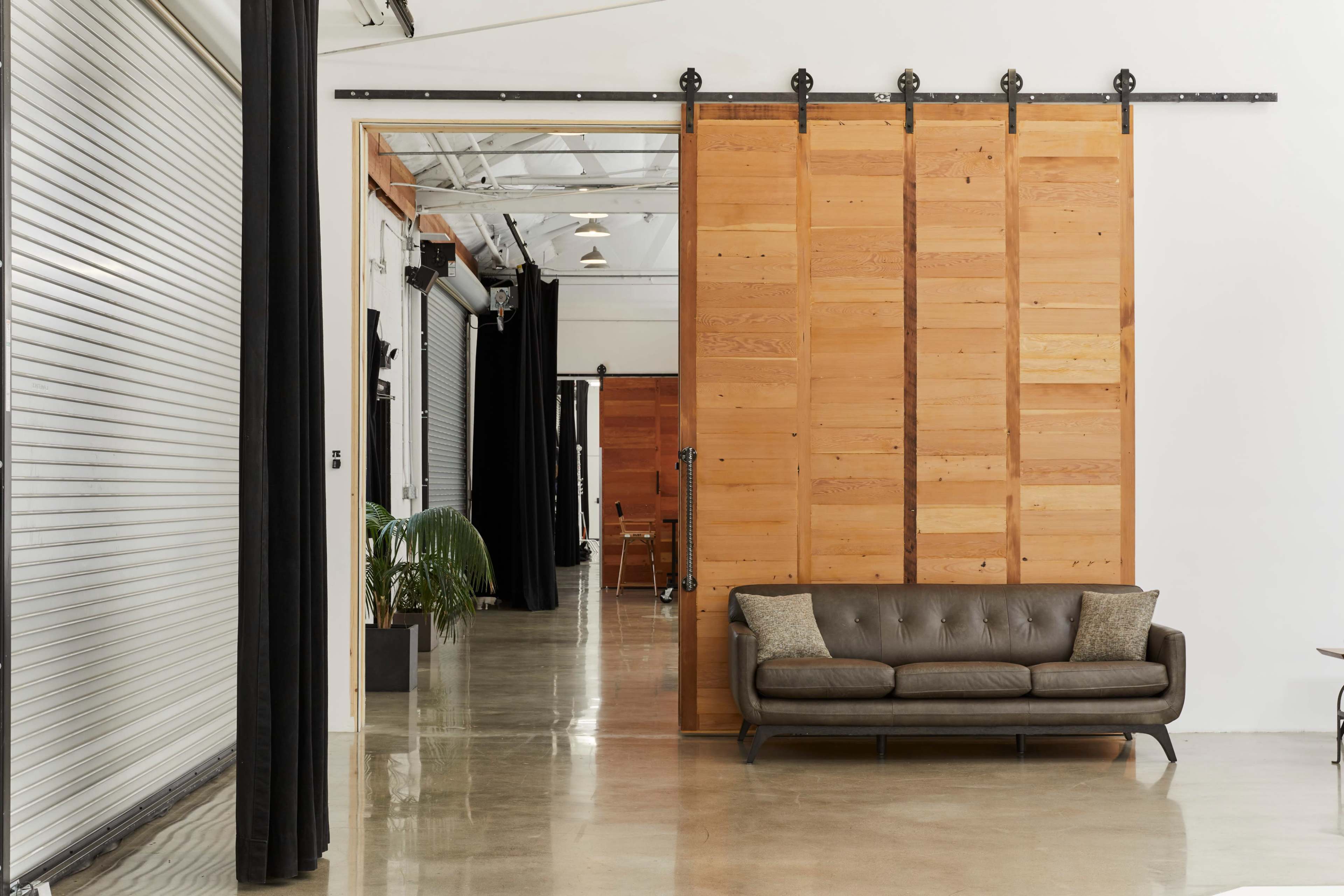 The image shows a modern interior space featuring a brown leather sofa and large wooden sliding doors on a minimalistic concrete floor.