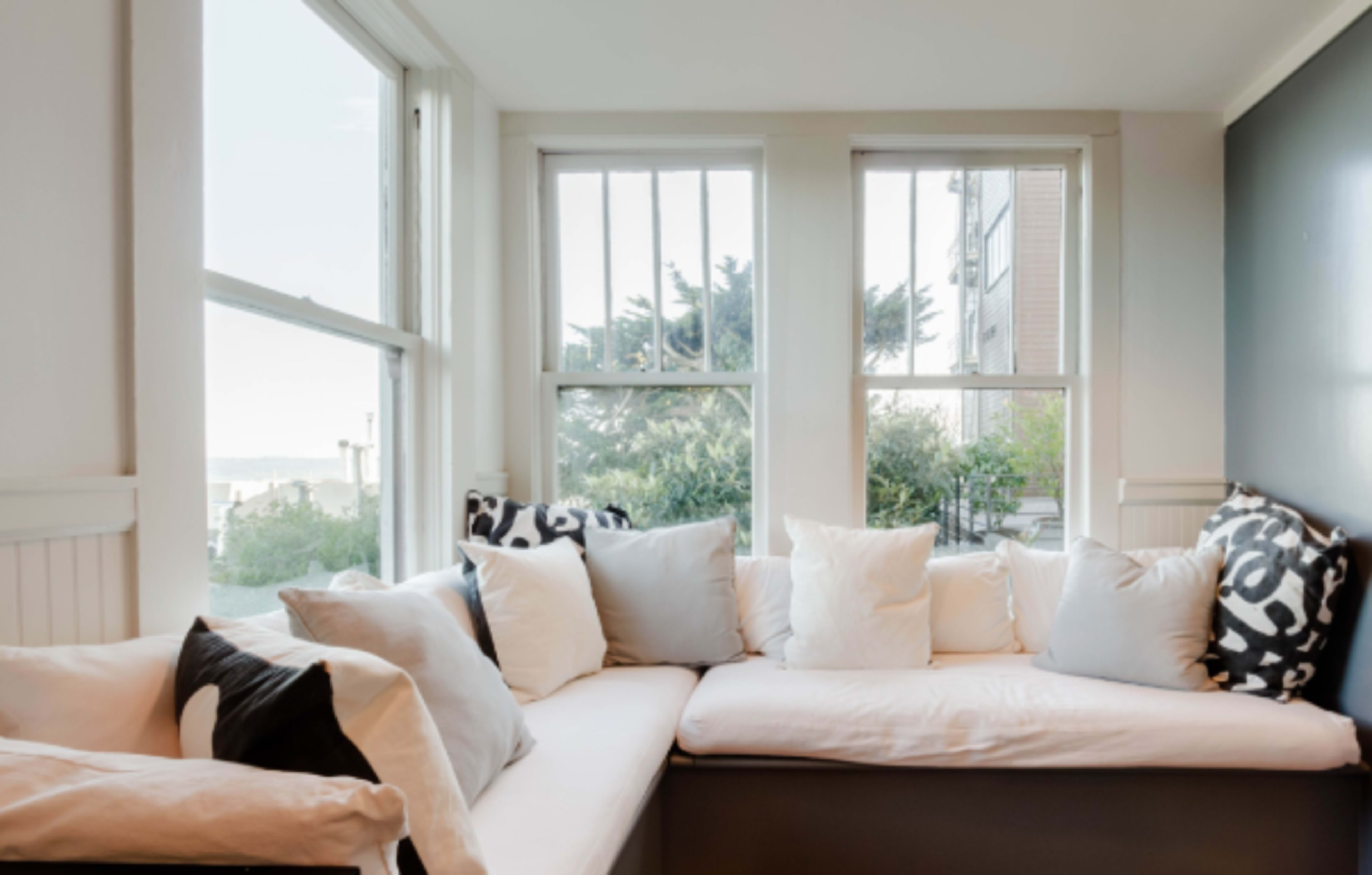 A cozy window seat is adorned with multiple cushions and provides a view of the outdoors through large windows.
