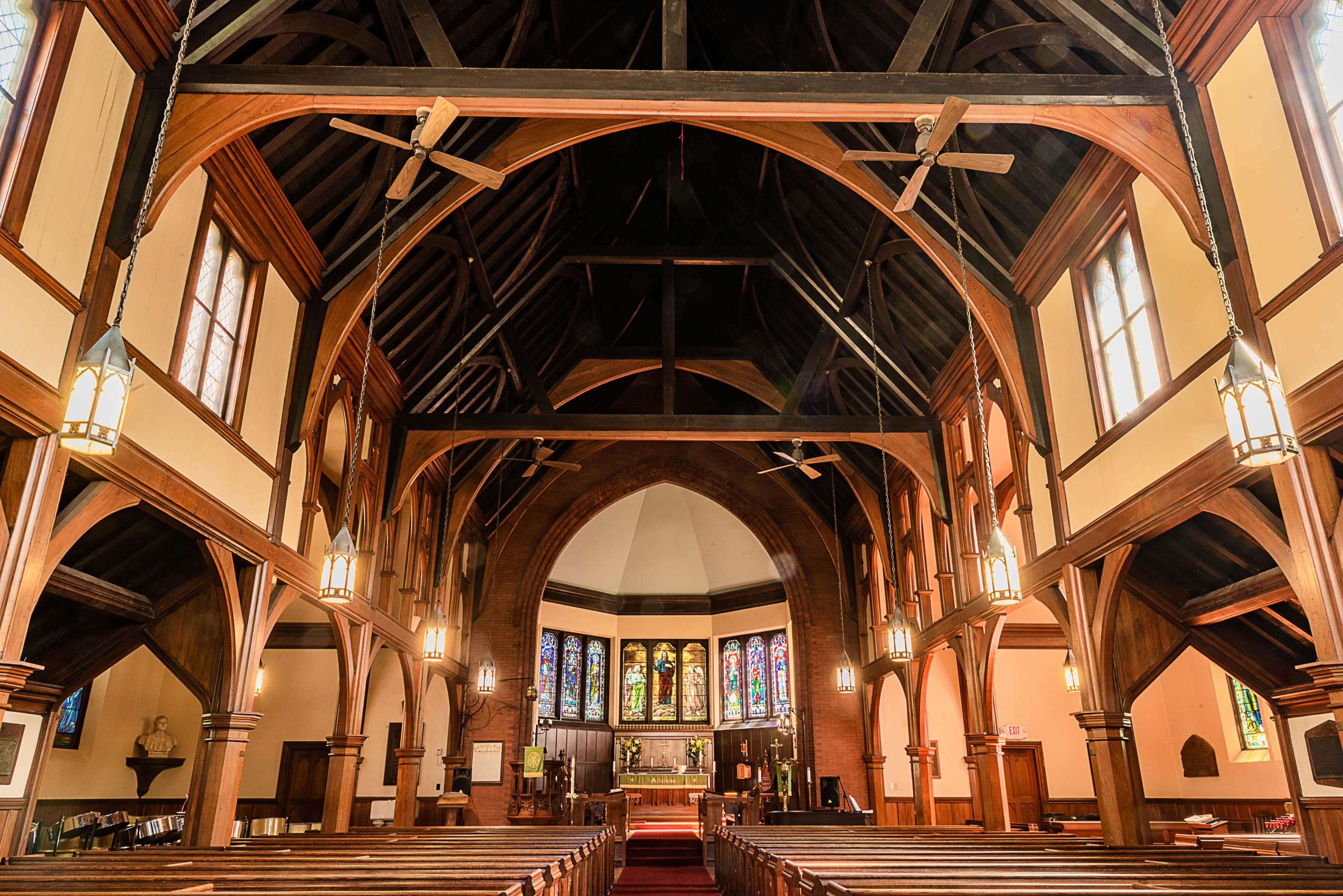 The interior of a church features high wooden beams, stained glass windows, and rows of wooden pews.