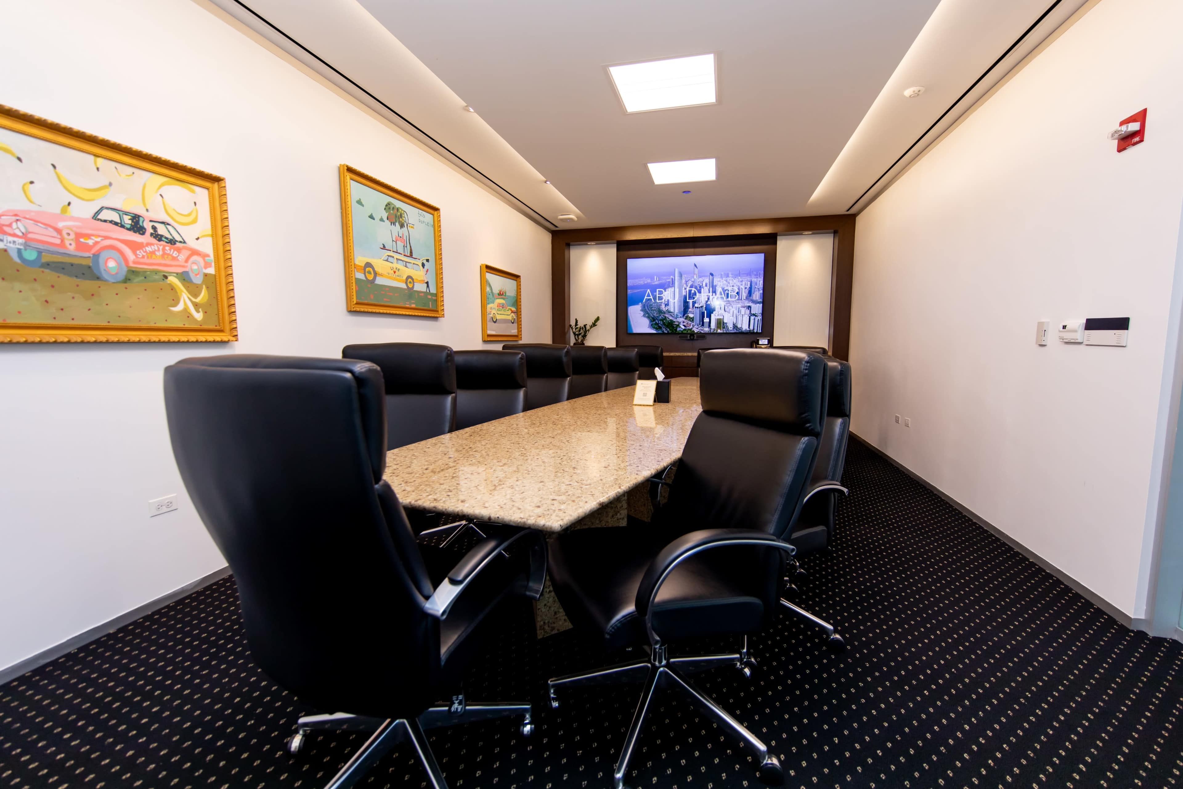 The image shows a modern conference room with a long granite table, black leather chairs, and framed artwork on the walls.