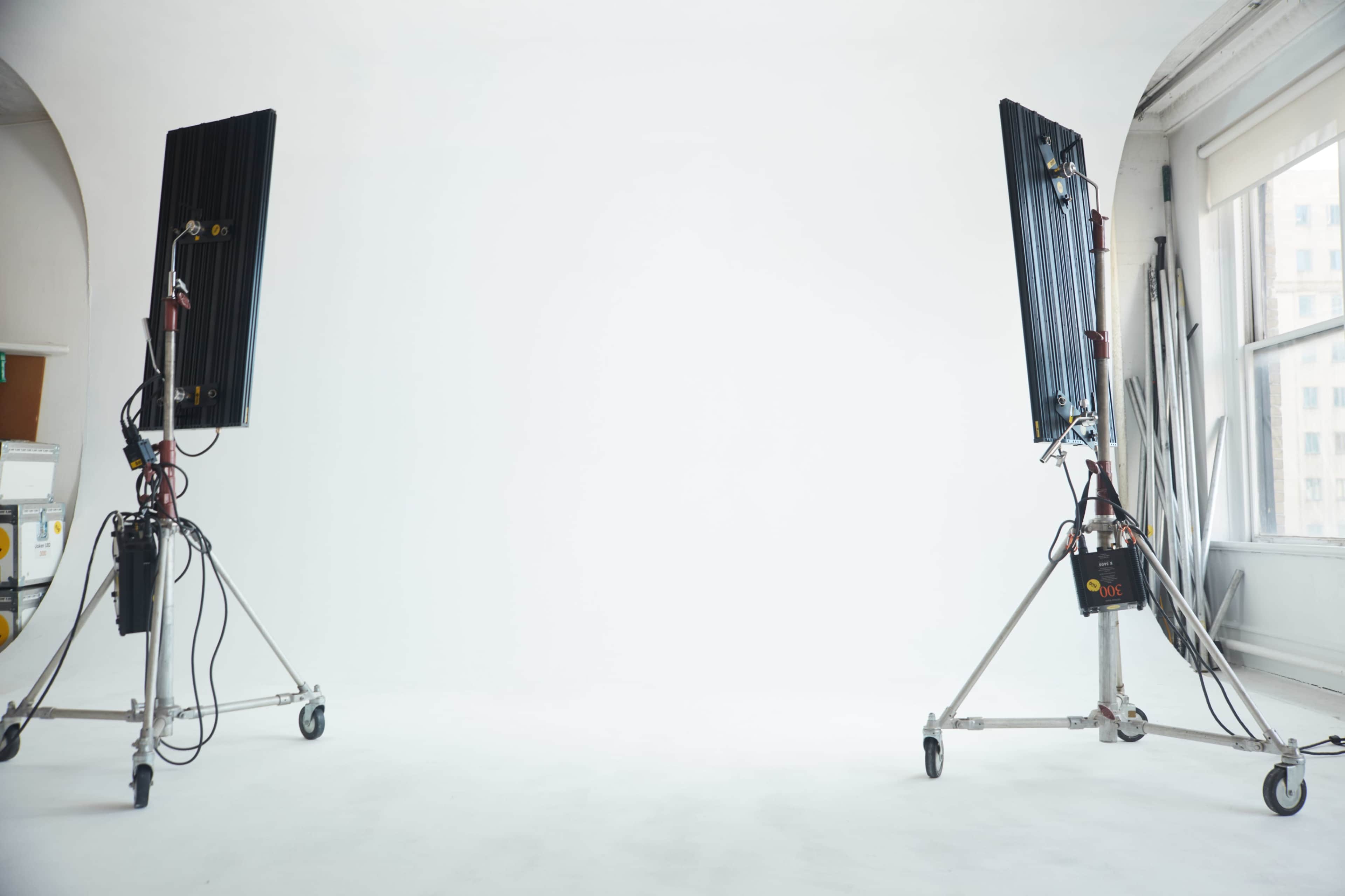 Two large lighting fixtures on stands are positioned opposite each other in a bright, empty studio space.