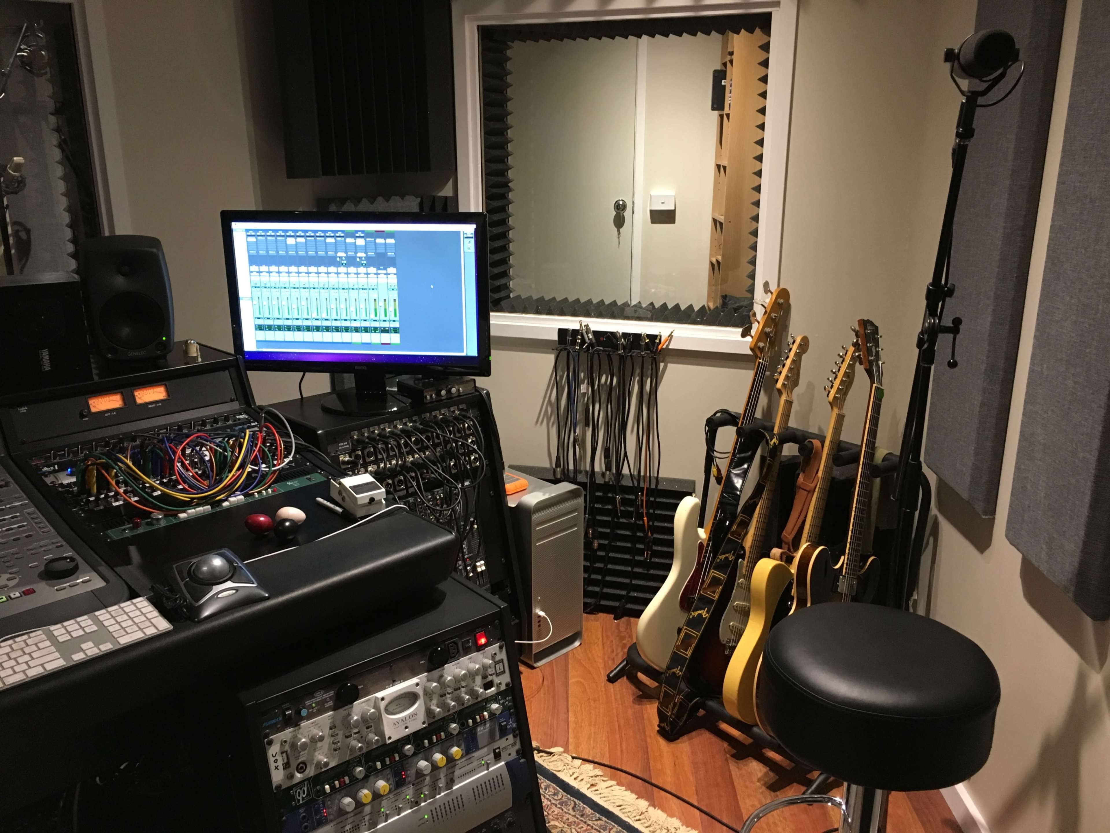 A recording studio with a computer monitor displaying audio tracks, various sound equipment, and several guitars leaning against a wall.