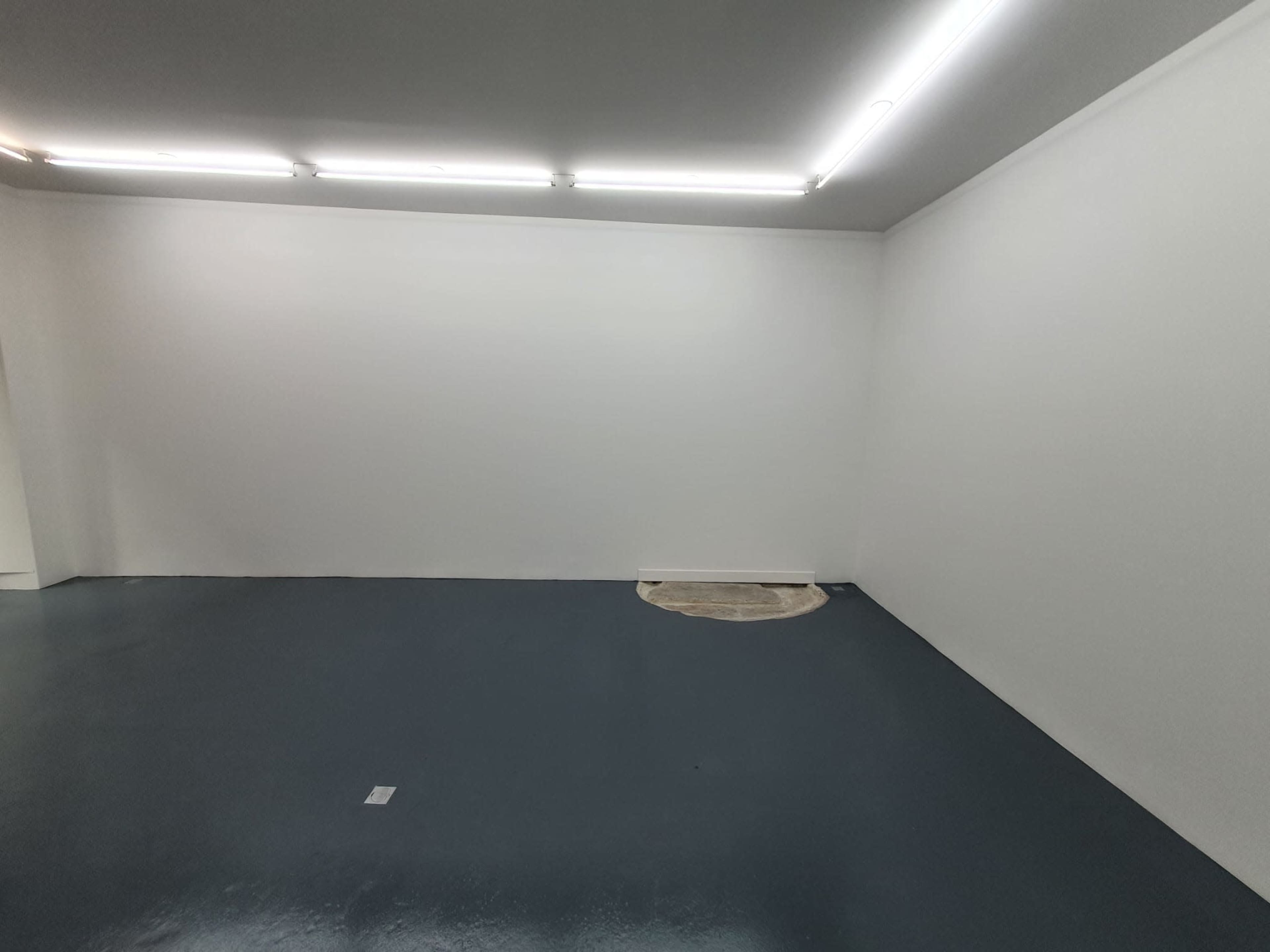 A vacant room with a gray floor and white walls, featuring a circular cutout in the corner.