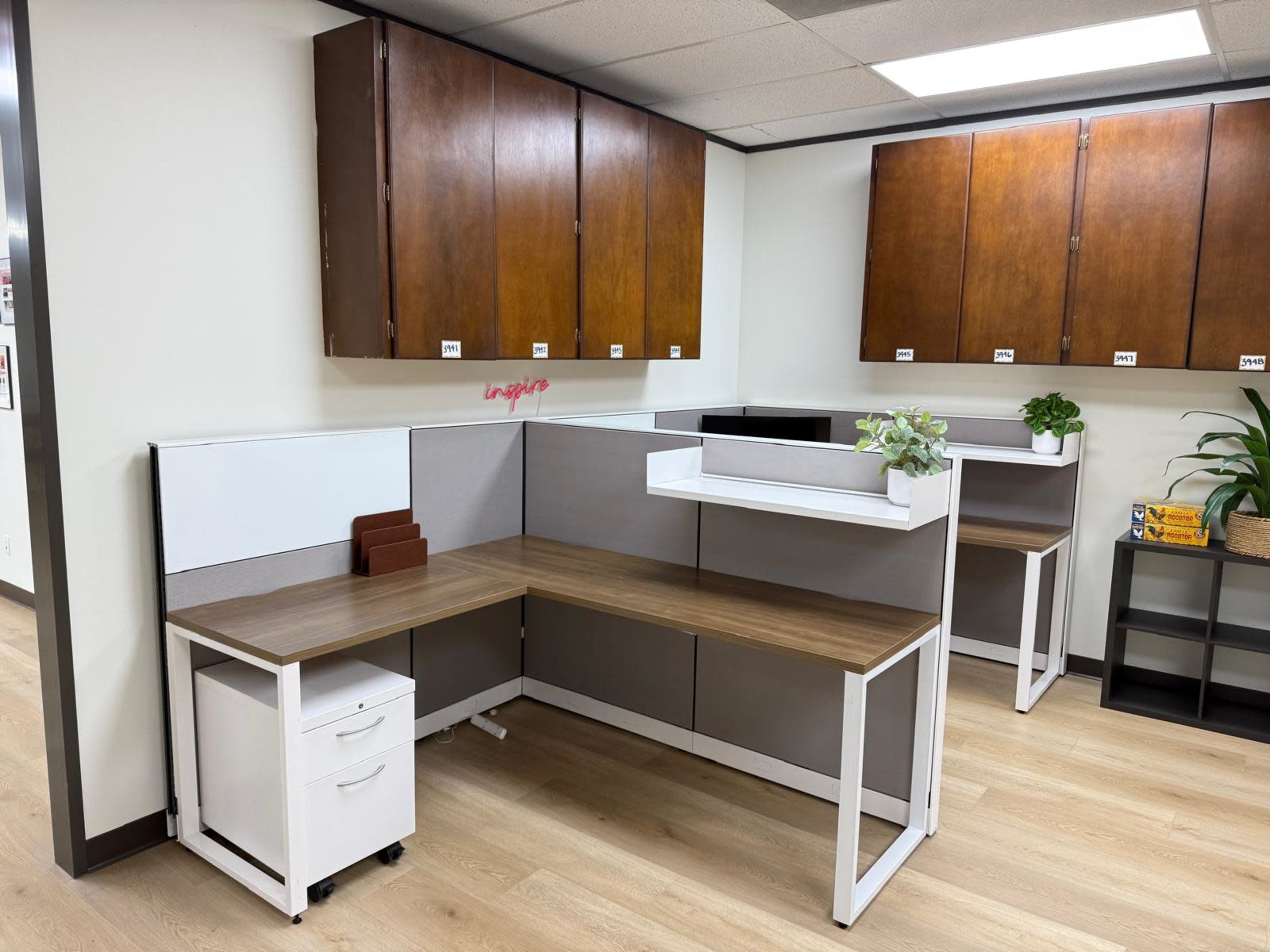The image shows a modern office space with two workstations separated by grey partitions and a small mobile filing cabinet.