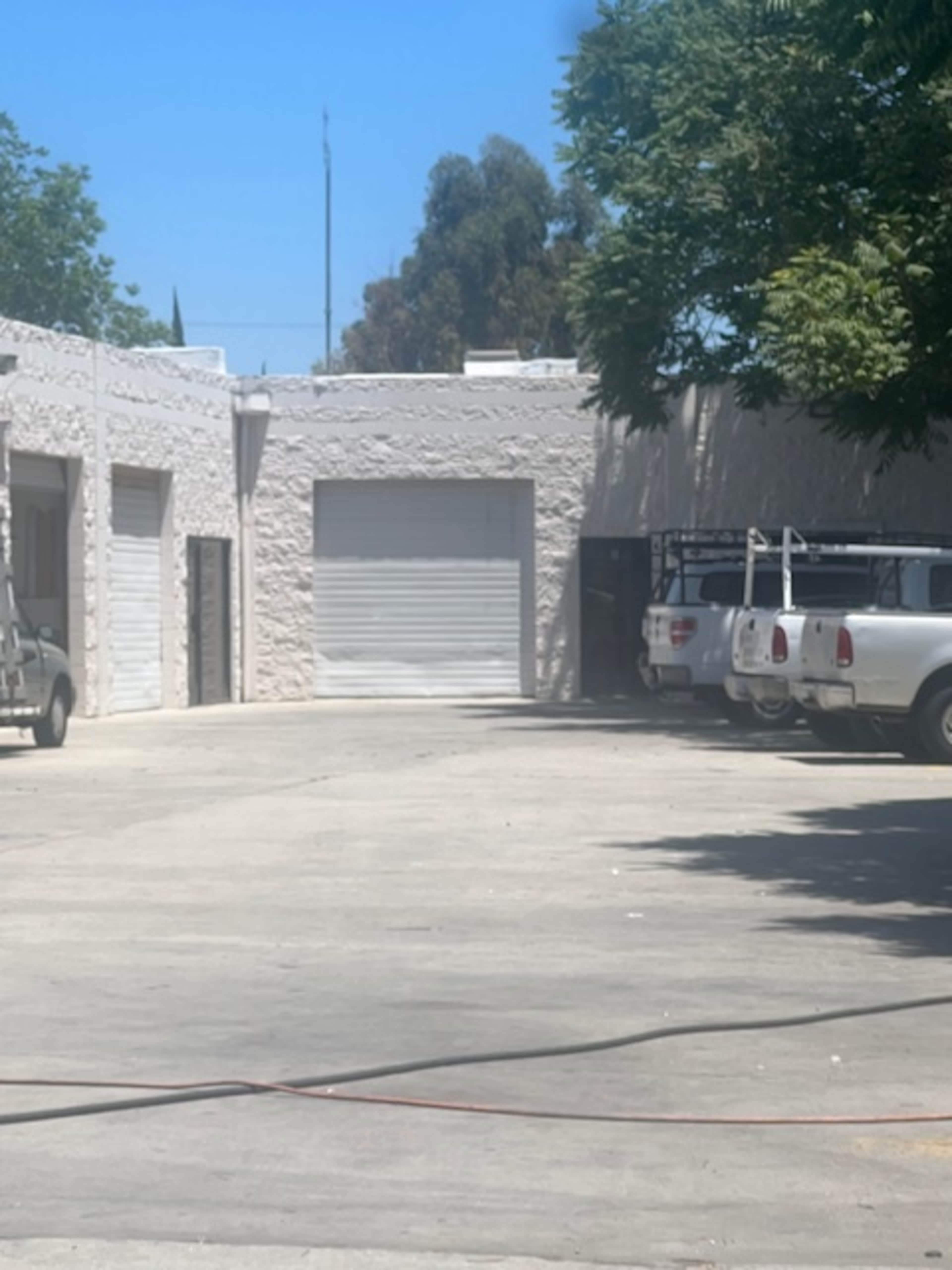 The image shows a concrete parking lot with several vehicles parked in front of a building featuring multiple roll-up garage doors.