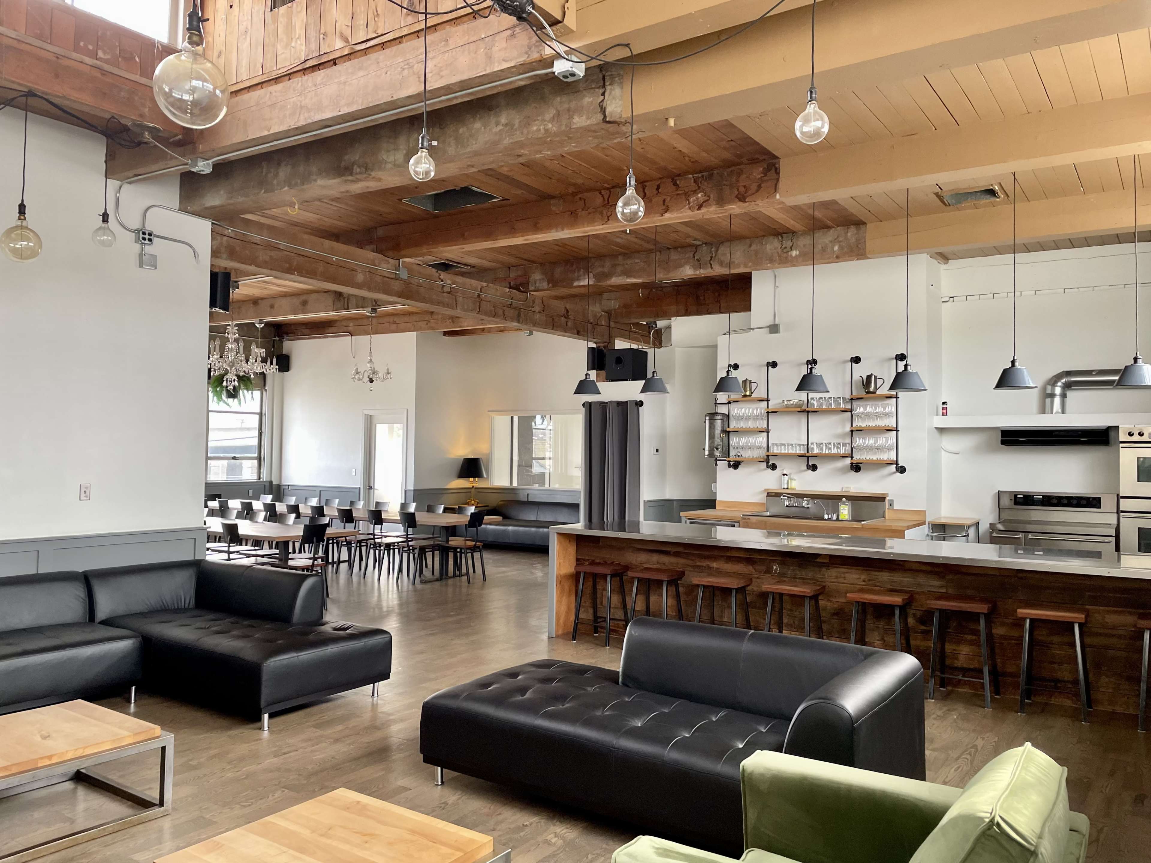 An interior space featuring a bar area with wooden counters, seating arrangements including sofas and tables, high ceilings with exposed beams, and pendant lighting.
