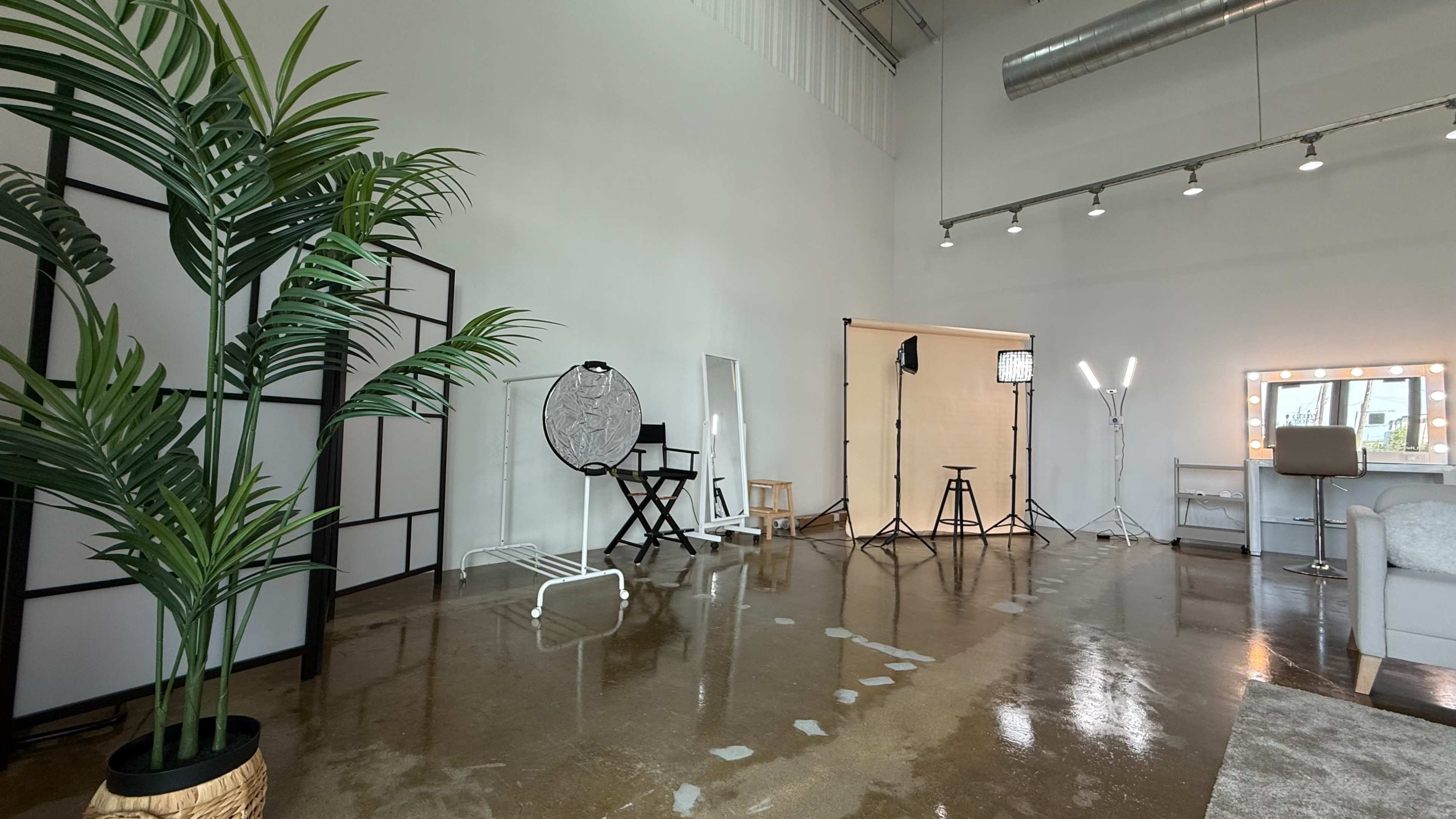 The image shows a studio space with a polished concrete floor, framed partitions, a makeup station, and various lighting equipment set up for photography or videography.
