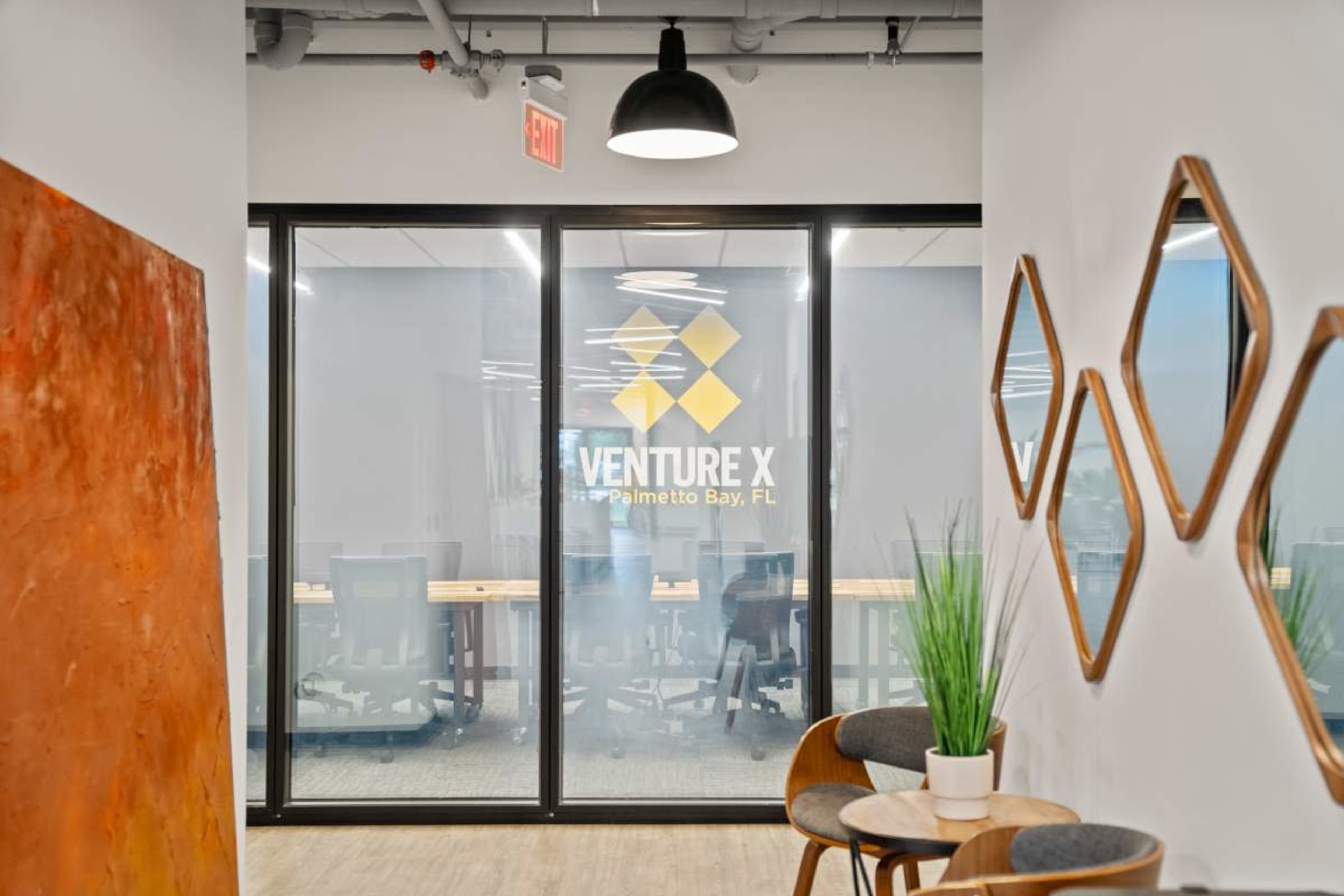 The image shows a modern office hallway leading to a glass-walled meeting room with the "VENTURE X" logo prominently displayed.