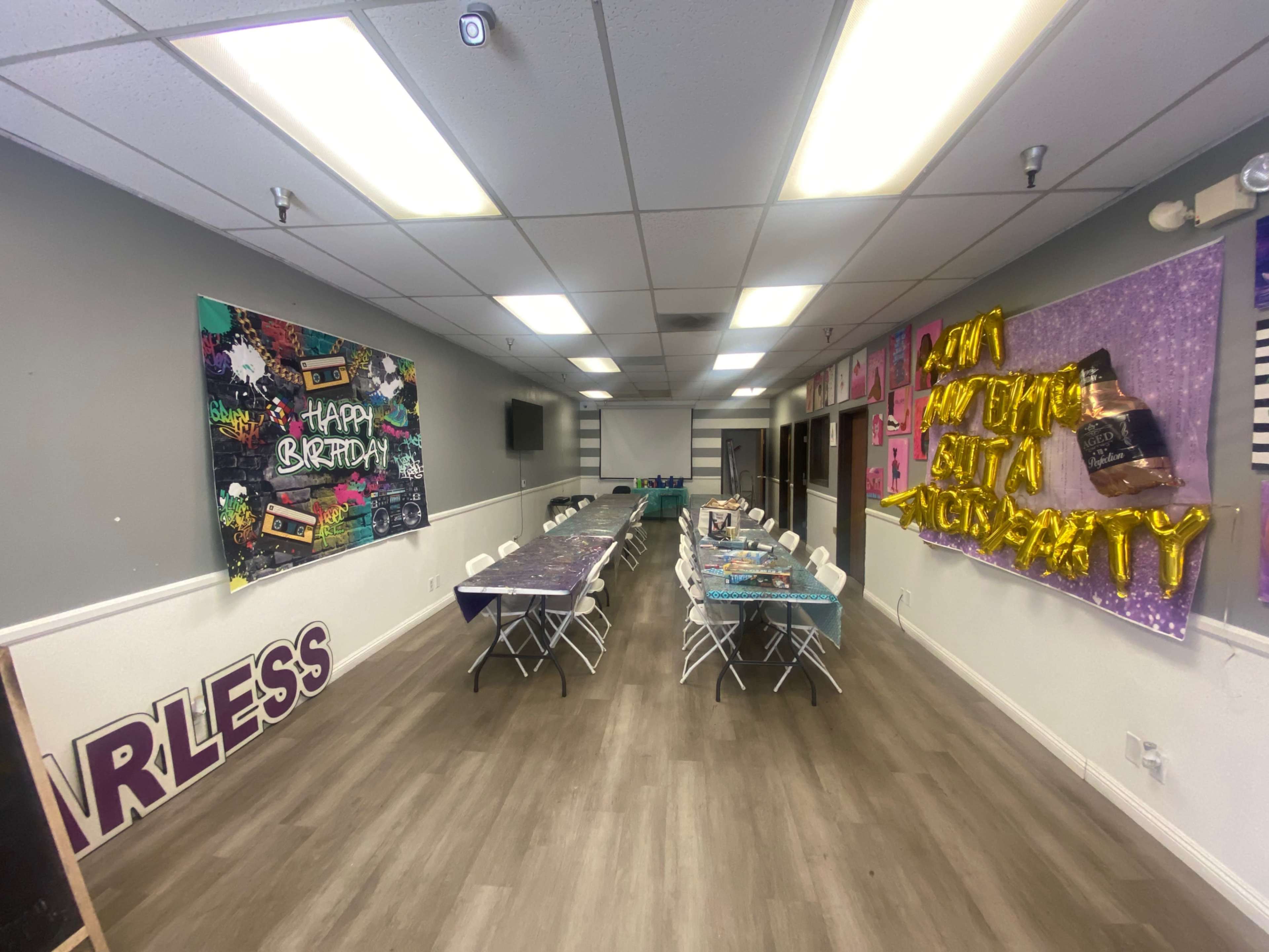 A decorated party room with tables set up for a birthday celebration, featuring colorful banners and table settings.