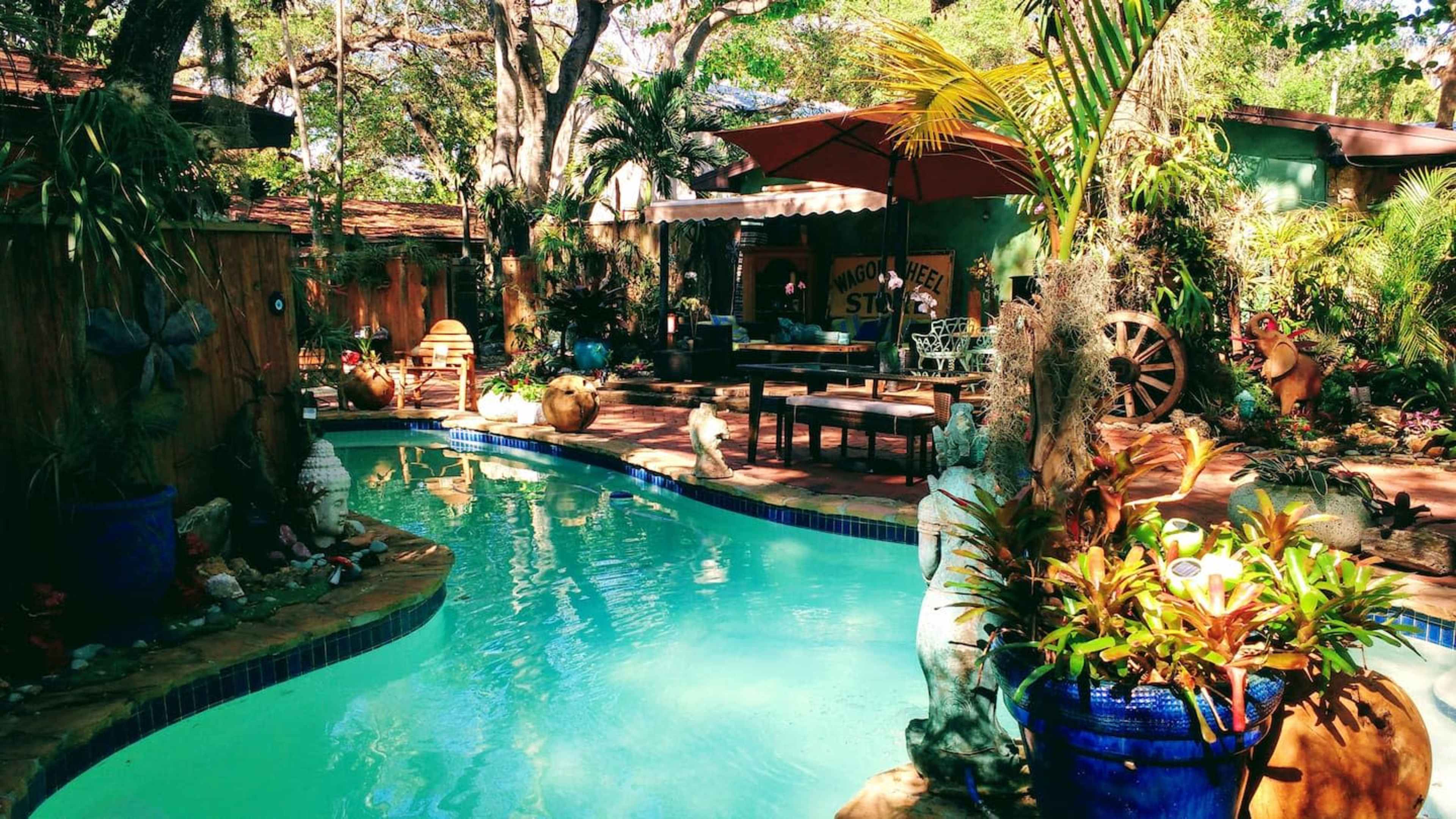 A vibrant garden with a swimming pool surrounded by lush greenery, decorative plants, and outdoor seating.