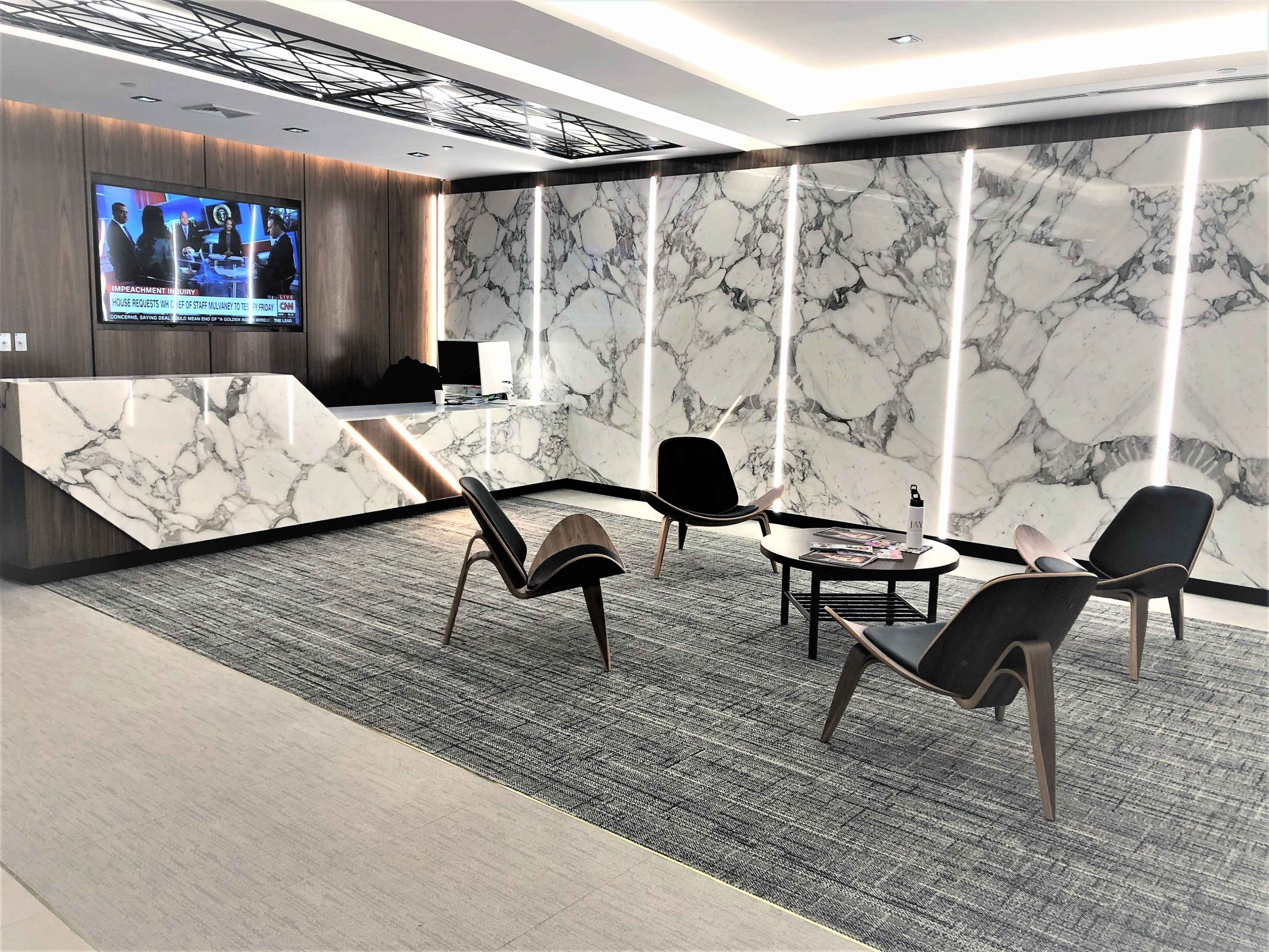 A modern reception area features marble walls, a large television displaying news, and stylish seating arranged around a coffee table.