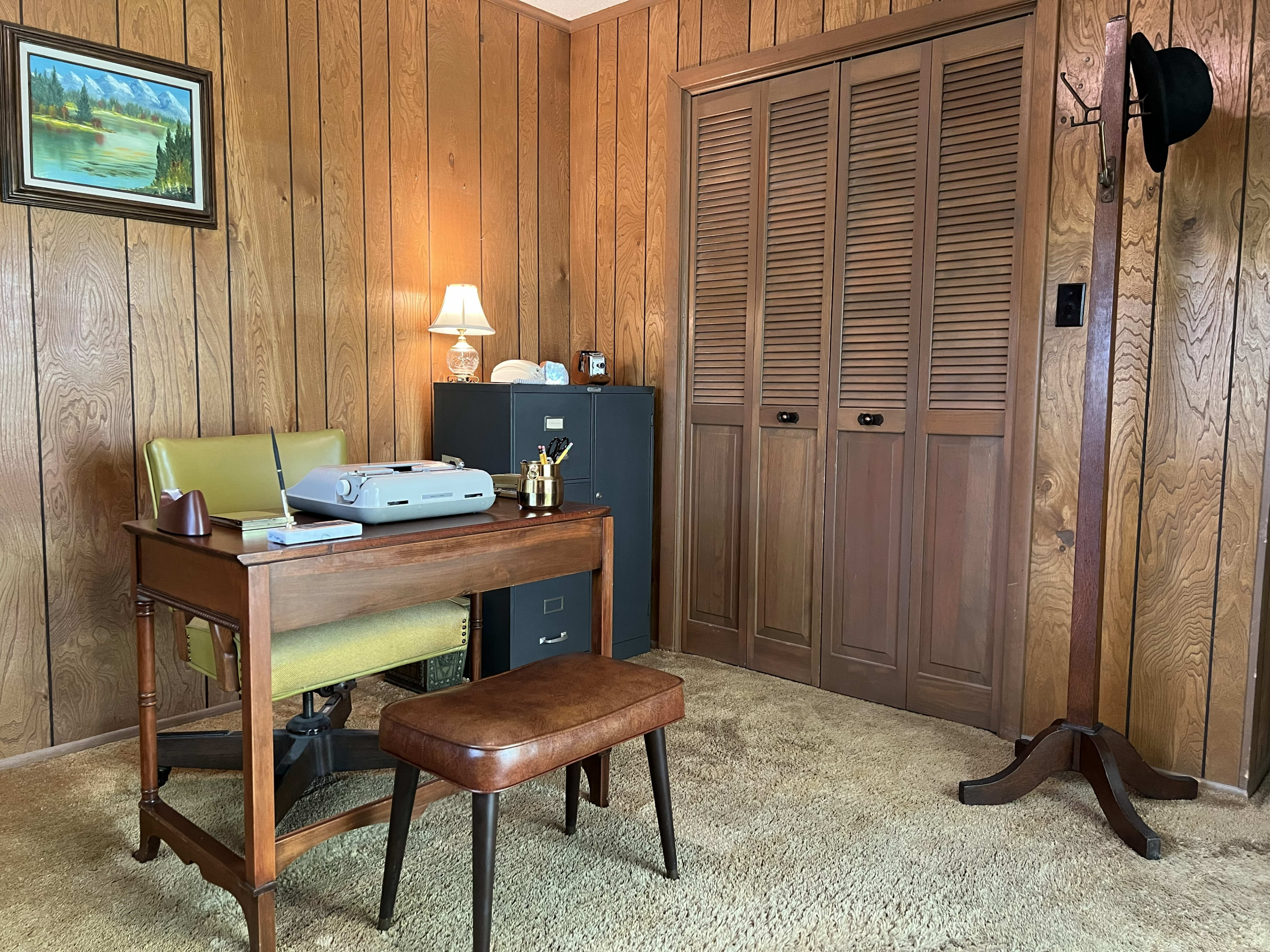 The image shows a vintage office with wood-paneled walls, a wooden desk, an office chair, a typewriter, and a coat rack.