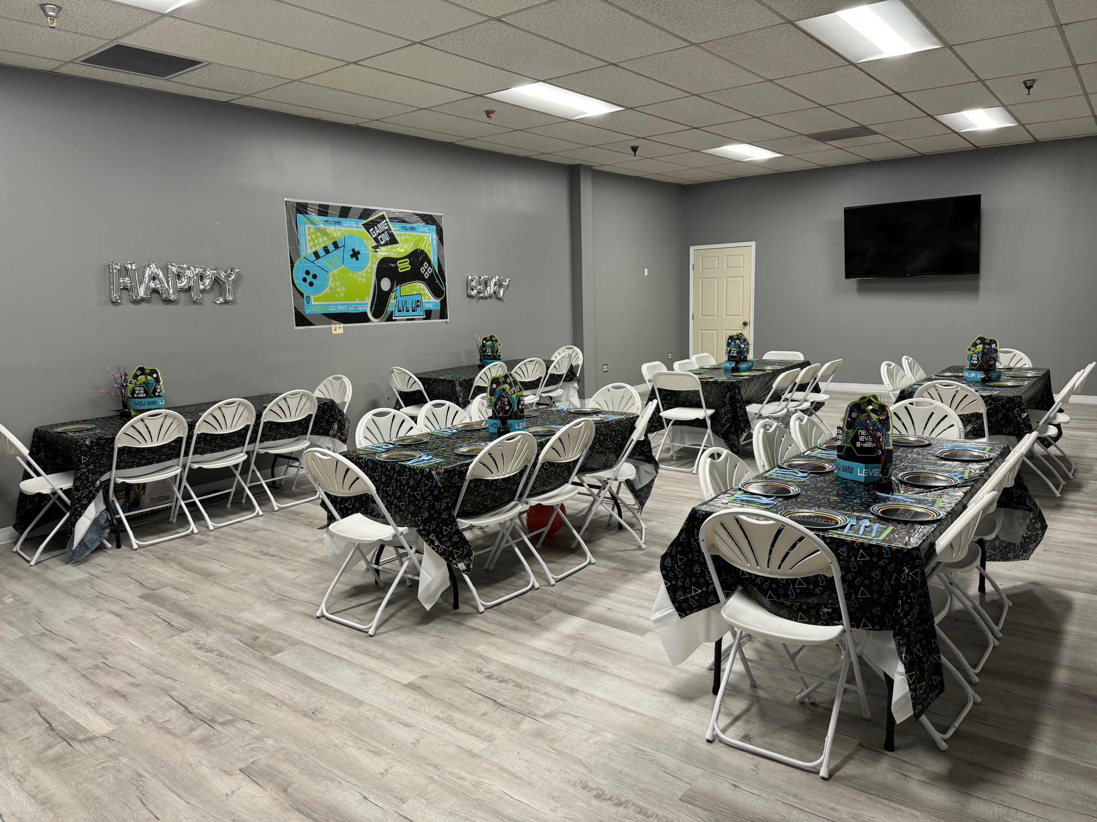 A decorated indoor party room with multiple tables set up for a celebration, featuring black and colorful tablecloths and themed centerpieces.