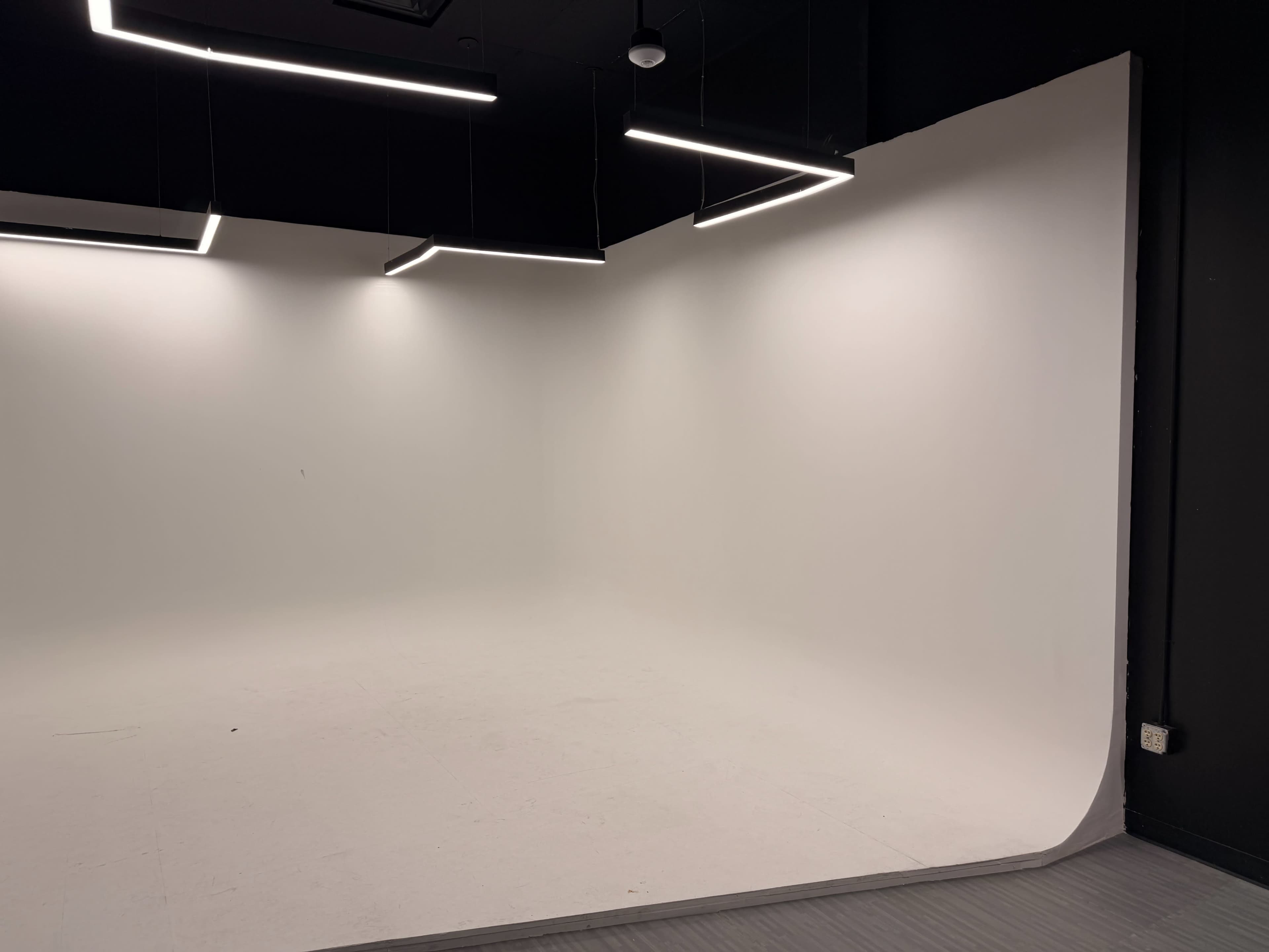 The image shows a modern photo studio with a seamless white backdrop and three overhead lights.