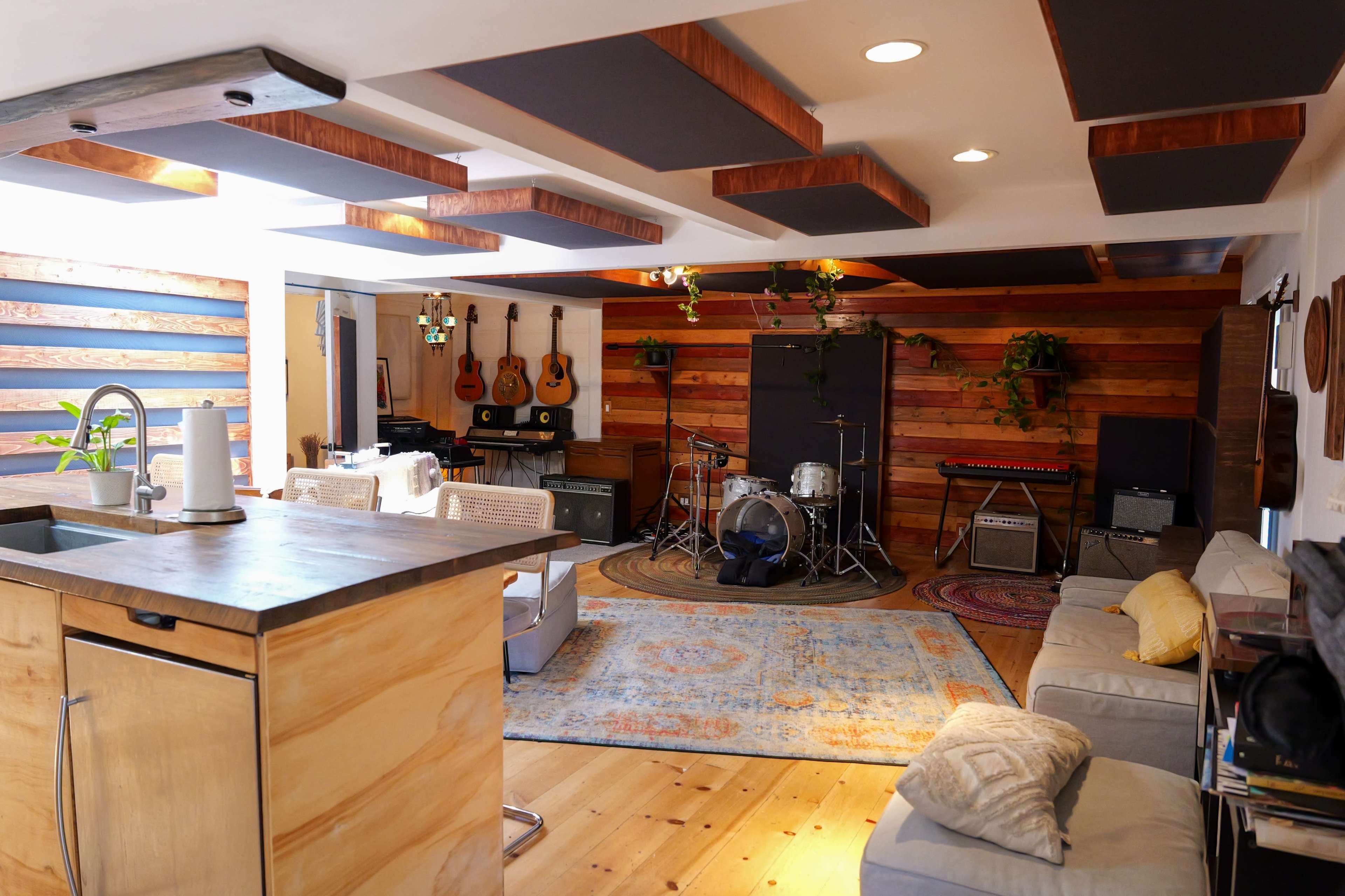 A spacious interior room with a music setup, featuring instruments, a seating area, and wooden accents on the walls and ceiling.