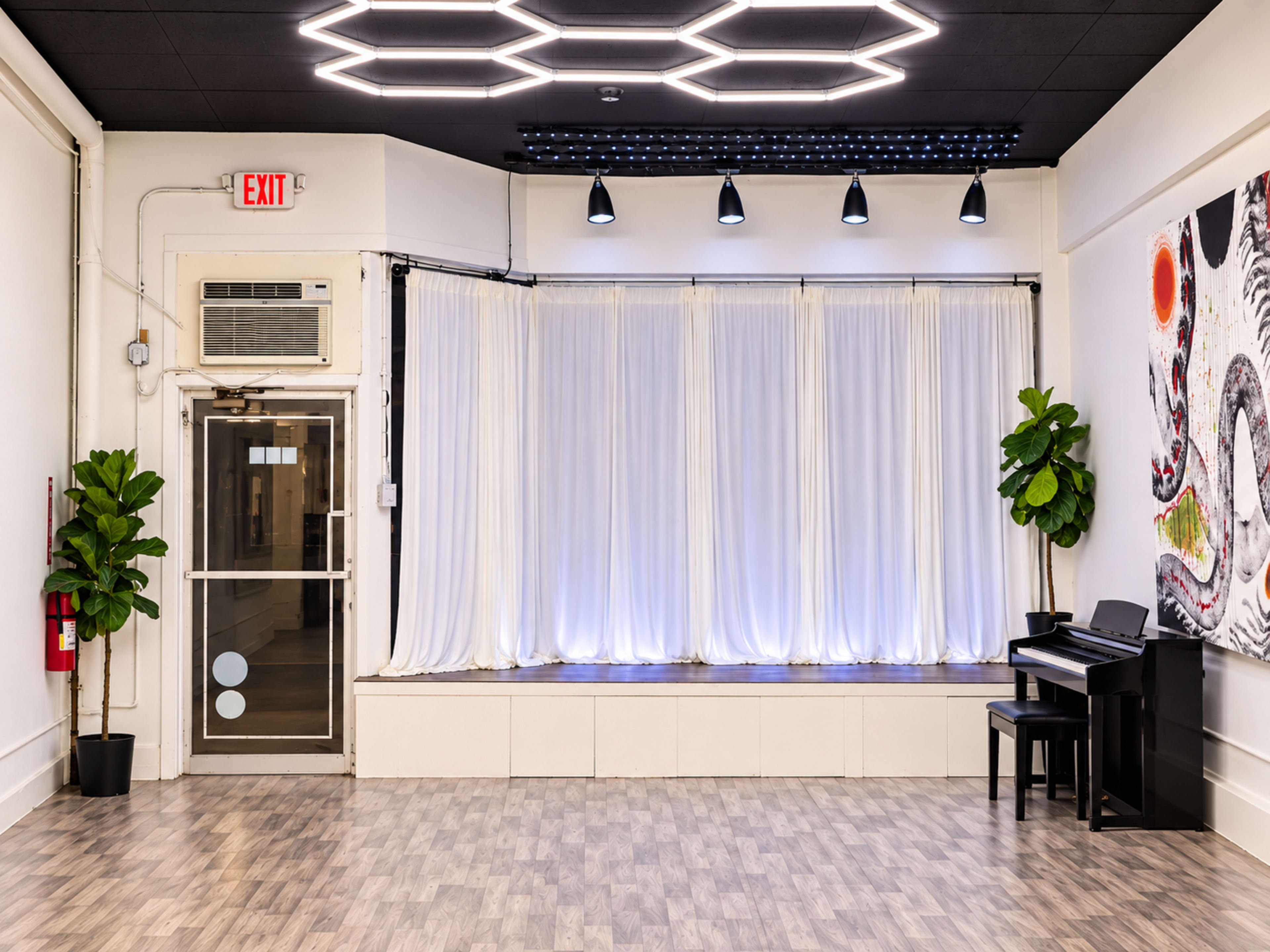 The image shows a spacious room with a grand piano, a large window draped with white curtains, and modern lighting fixtures on the ceiling.