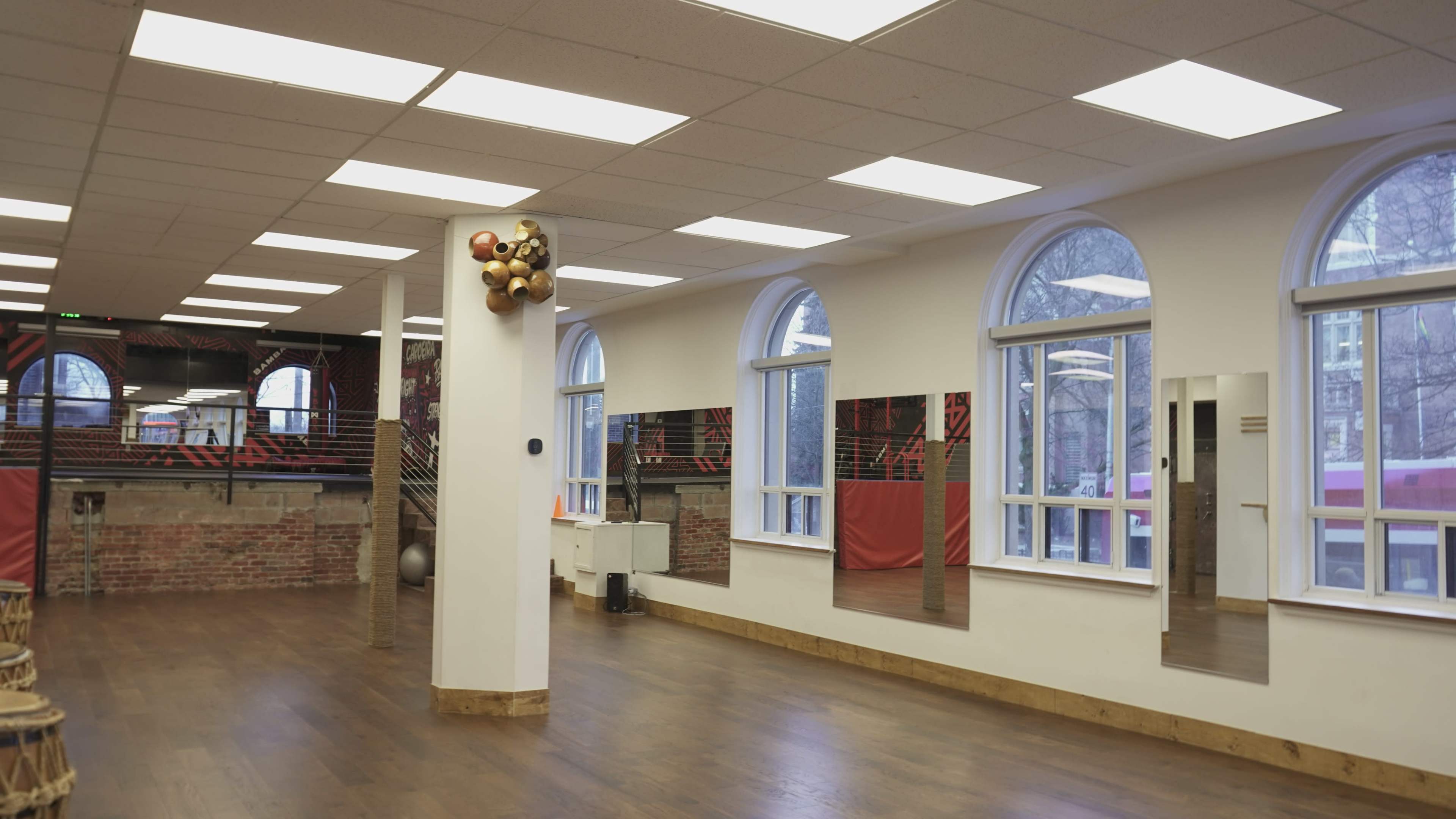 A spacious, well-lit studio with wooden flooring, large windows, and mirrored walls.