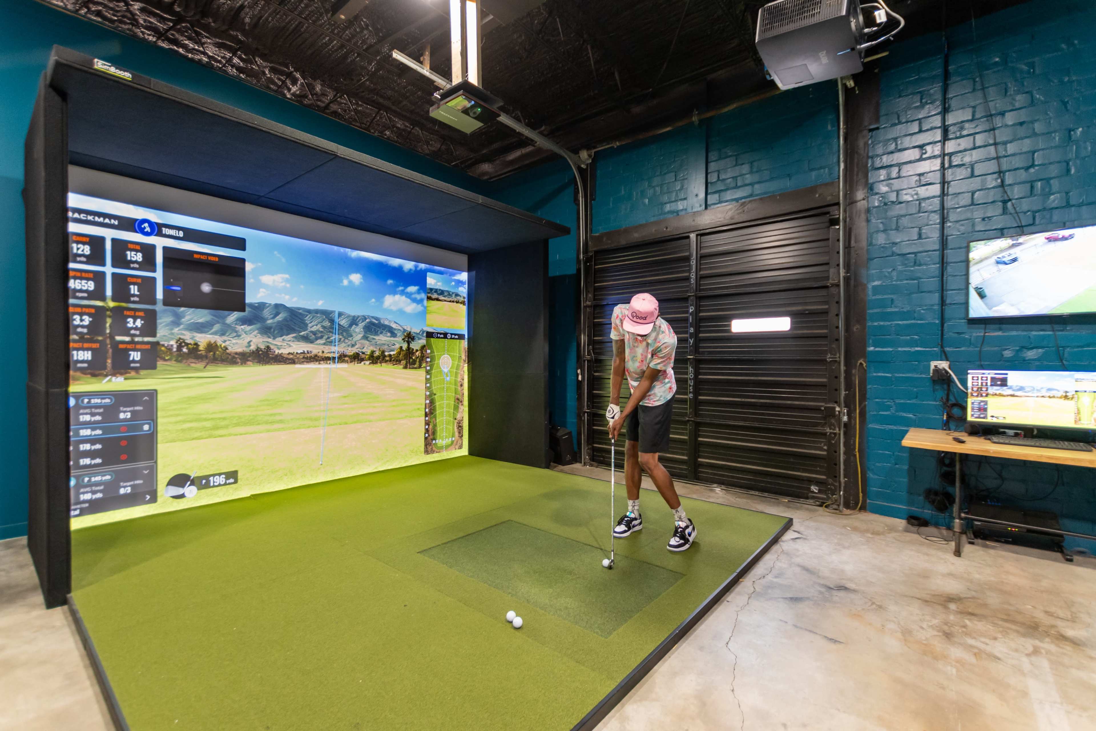 A person stands on a green mat in front of a large screen displaying a golf course, preparing to take a shot with a golf club.