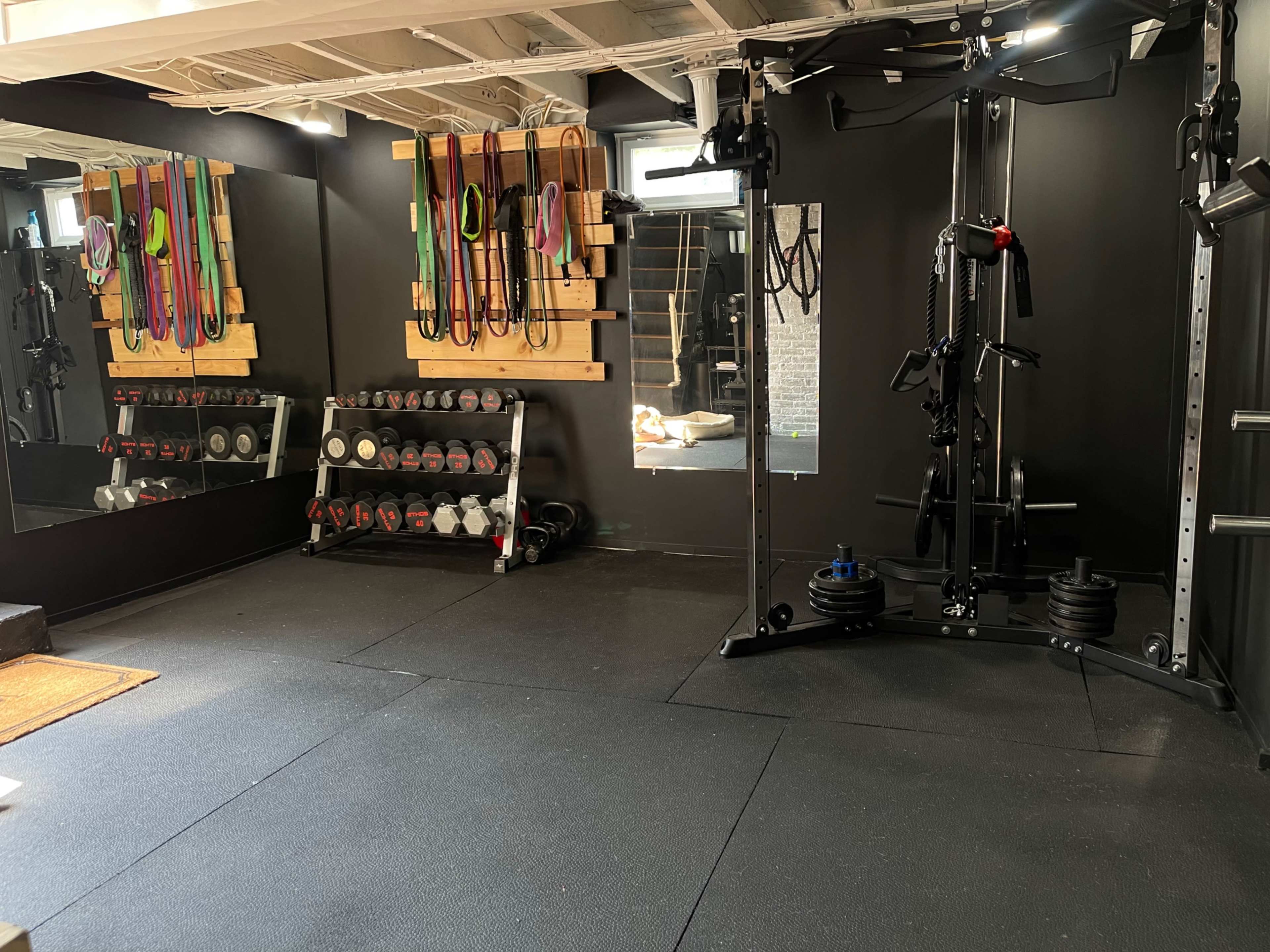 A home gym featuring various exercise equipment, including free weights, resistance bands mounted on the wall, and a multi-station workout machine.