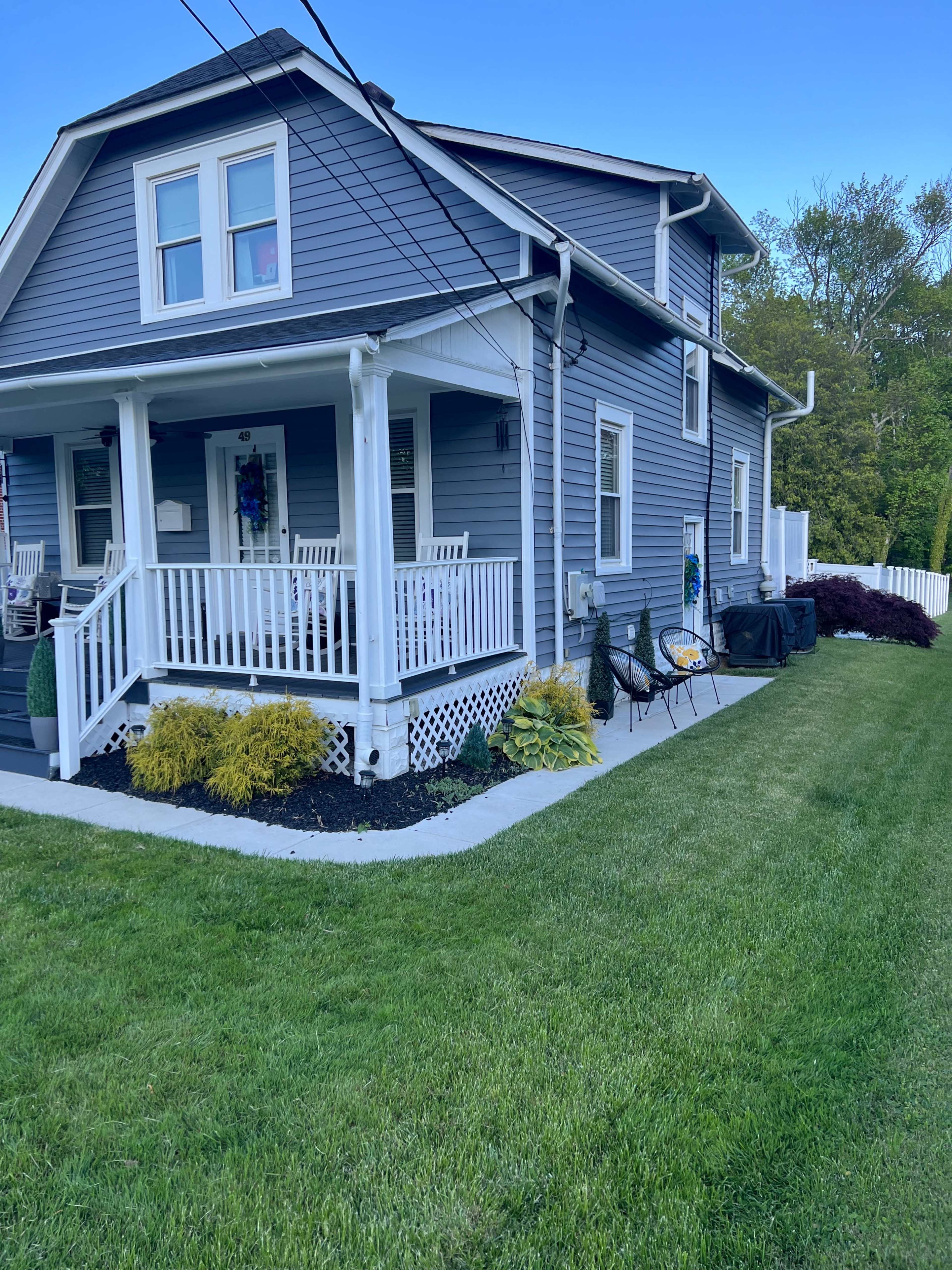 A two-story blue house with a front porch, surrounded by a well-manicured lawn and a small garden.