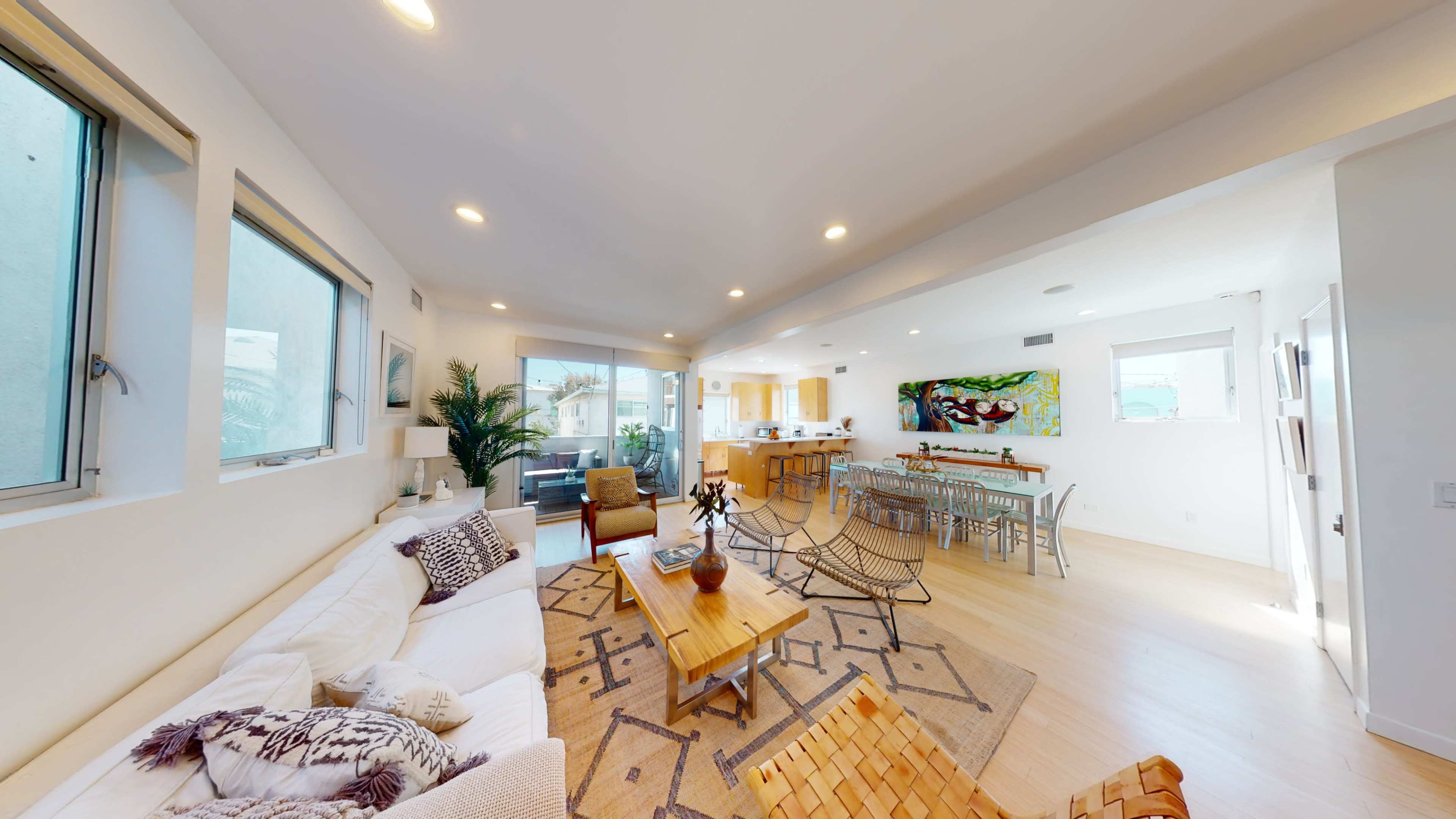 A modern, open-concept living and dining area with large windows, light-colored walls, and contemporary furniture.