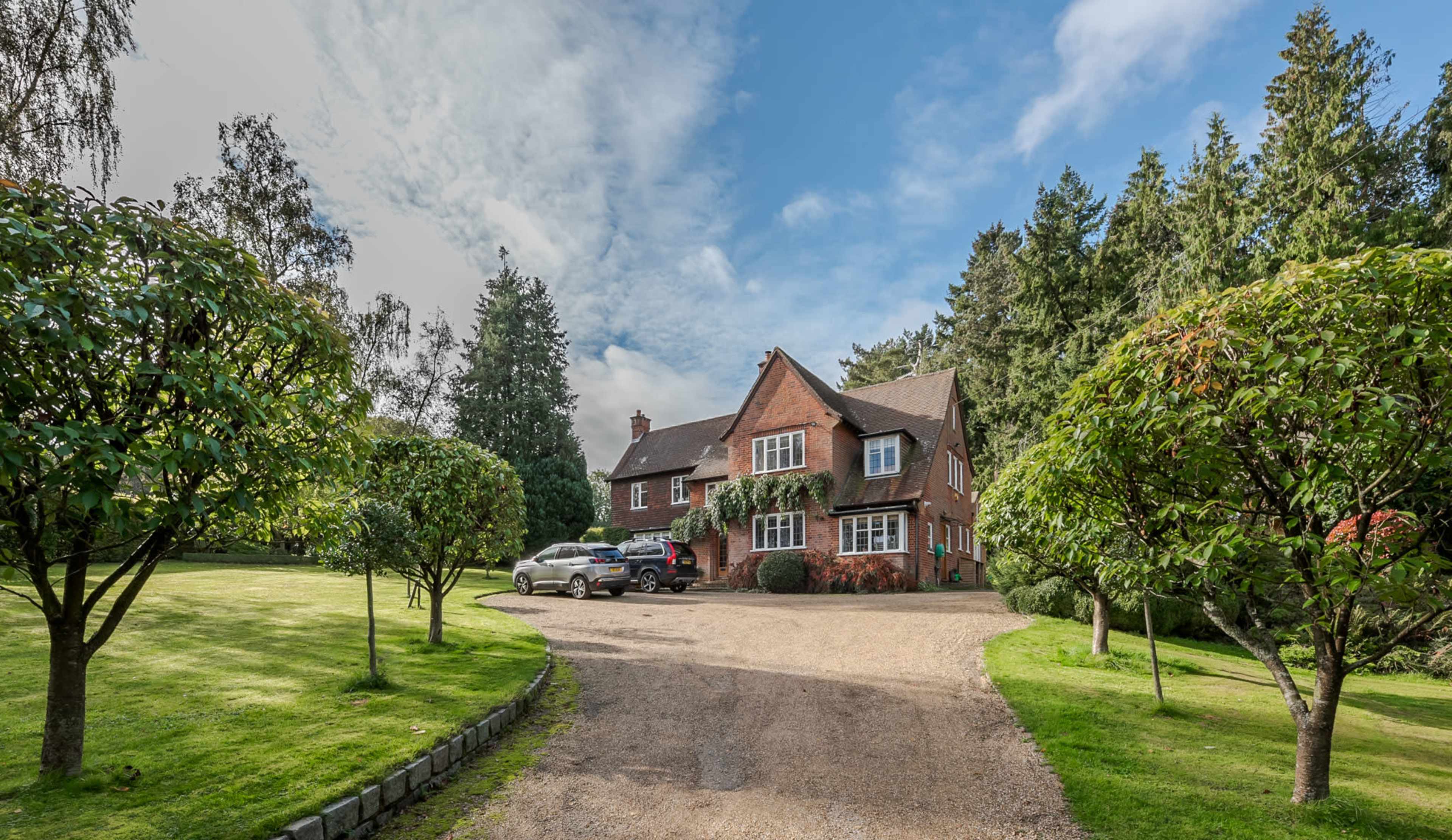 A spacious brick house is set alongside a gravel driveway, surrounded by neatly trimmed grass and trees.