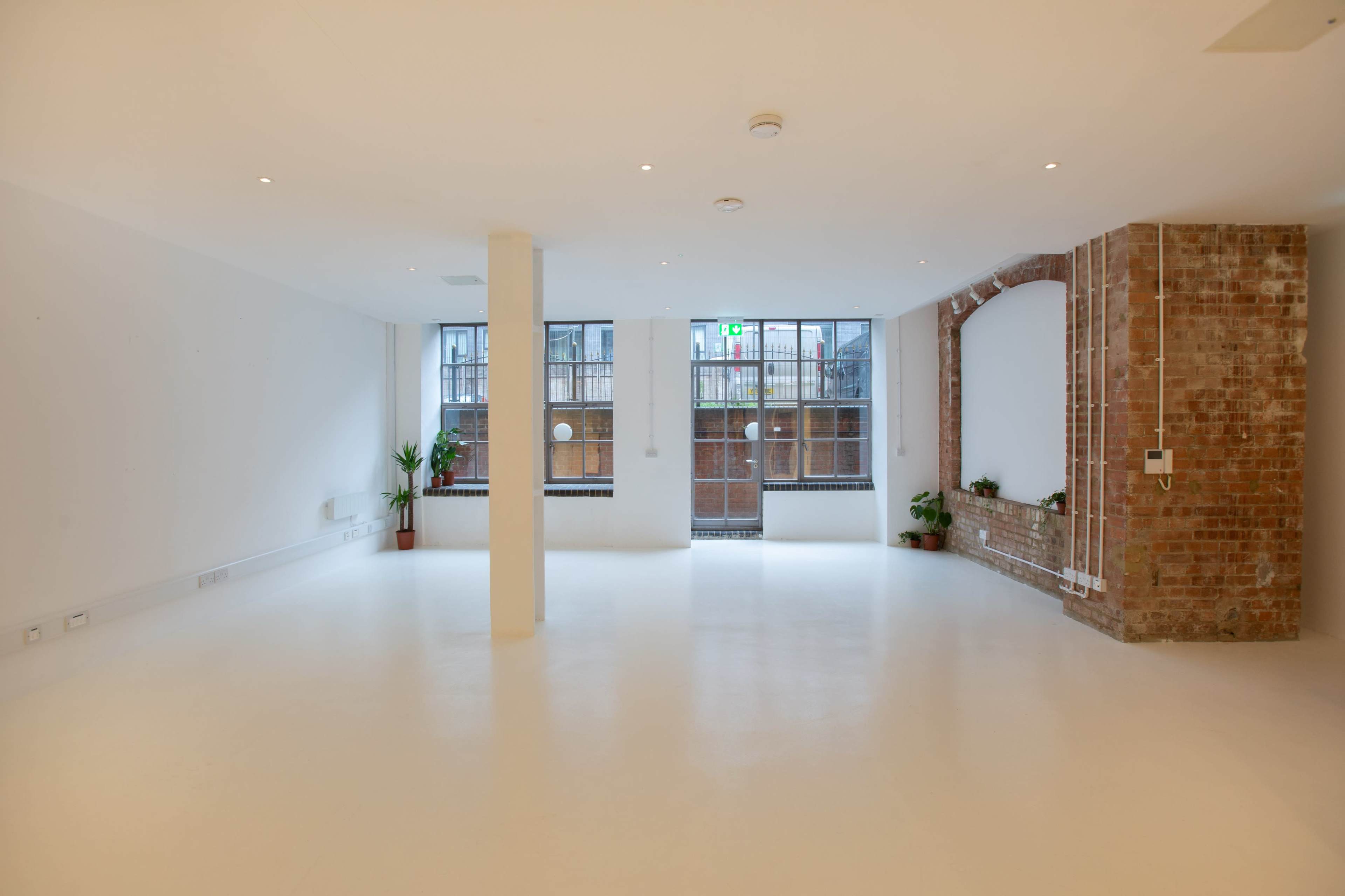 A spacious, empty room with white walls, large windows, and a brick feature wall.